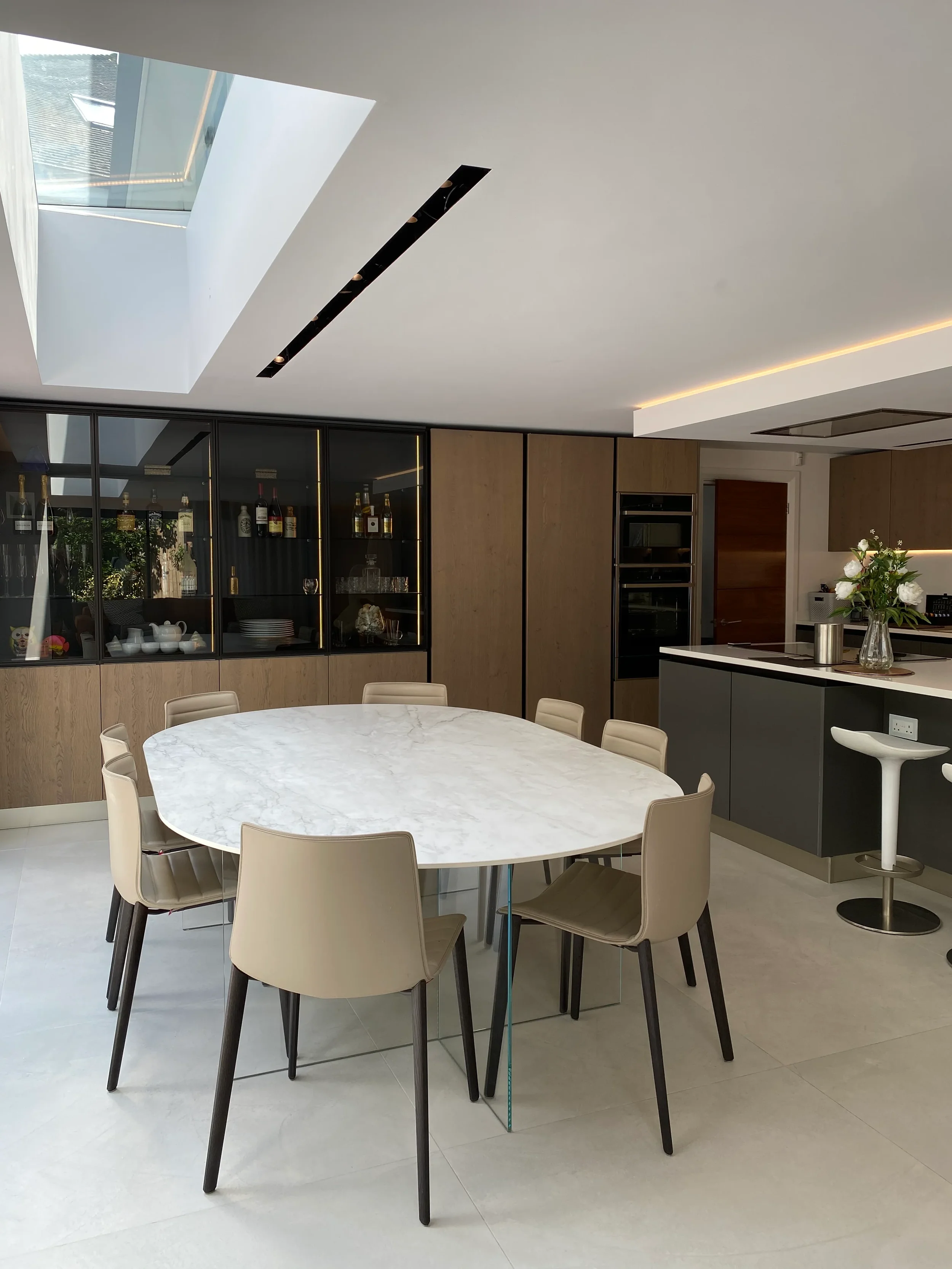 High-end modern interior showcasing premium custom porcelain furniture fabrication, highlighting a seamless stone-look porcelain dining table top integrated into an open-plan kitchen and living design with oak veneer cabinetry.
