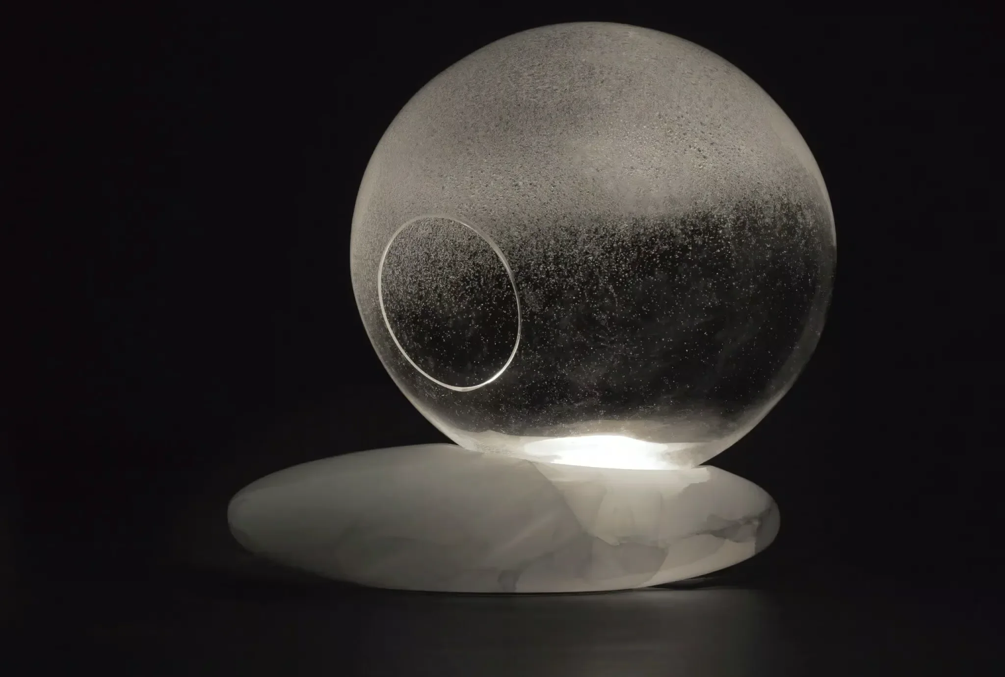 The Litia table lamp by Kreoo, designed by Enzo Berti, featuring a hand-blown Murano glass sphere with air bubbles set on an asymmetrical polished onyx base, available through PietraCasa.