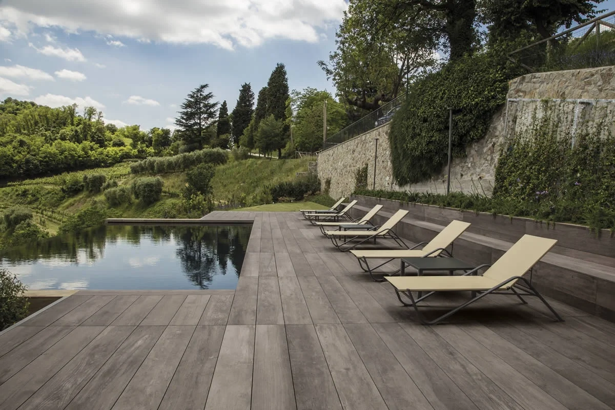 A stylish poolside area featuring Kronos Ceramiche's Wood Side collection, specifically the Oak 2.0 Essence in 2cm thickness, available through PietraCasa.