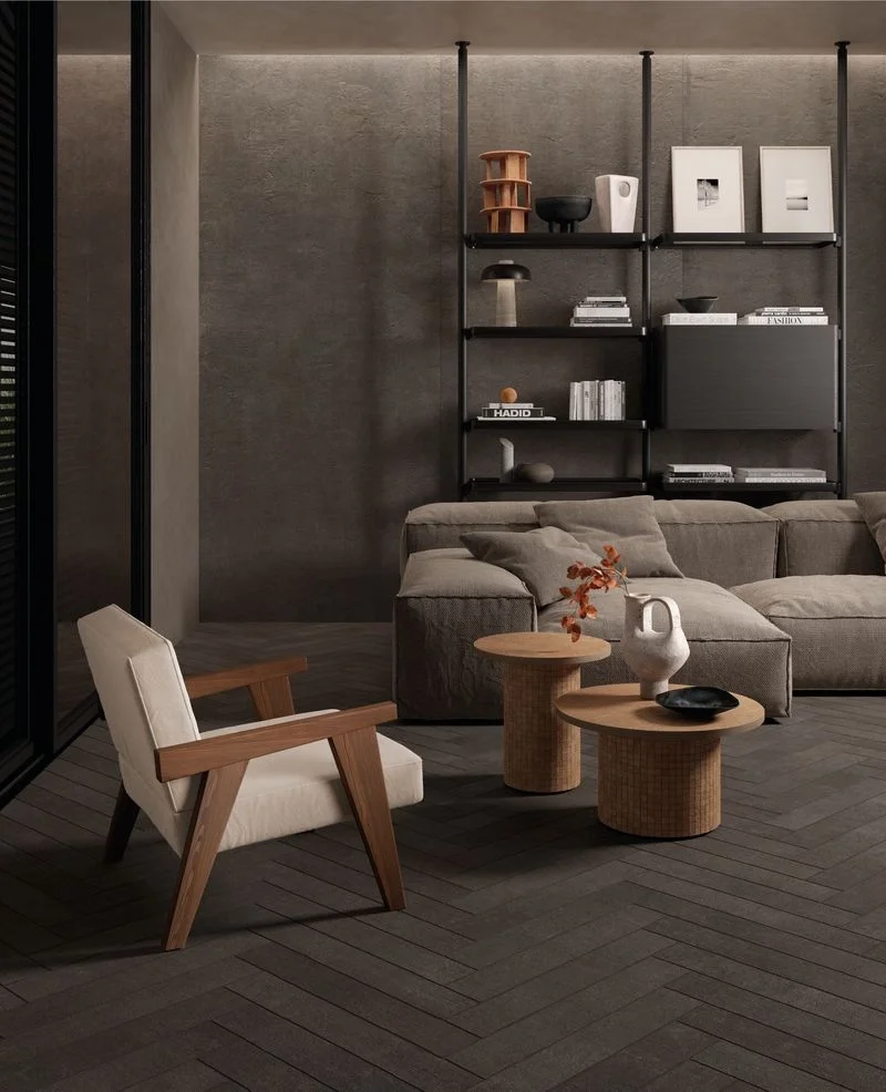 A modern living space featuring the Kronos Terra Crea porcelain stoneware collection, capturing the texture of raw earth and terracotta in a dark, structured tile laid in a classic chevron or herringbone pattern, available through PietraCasa.