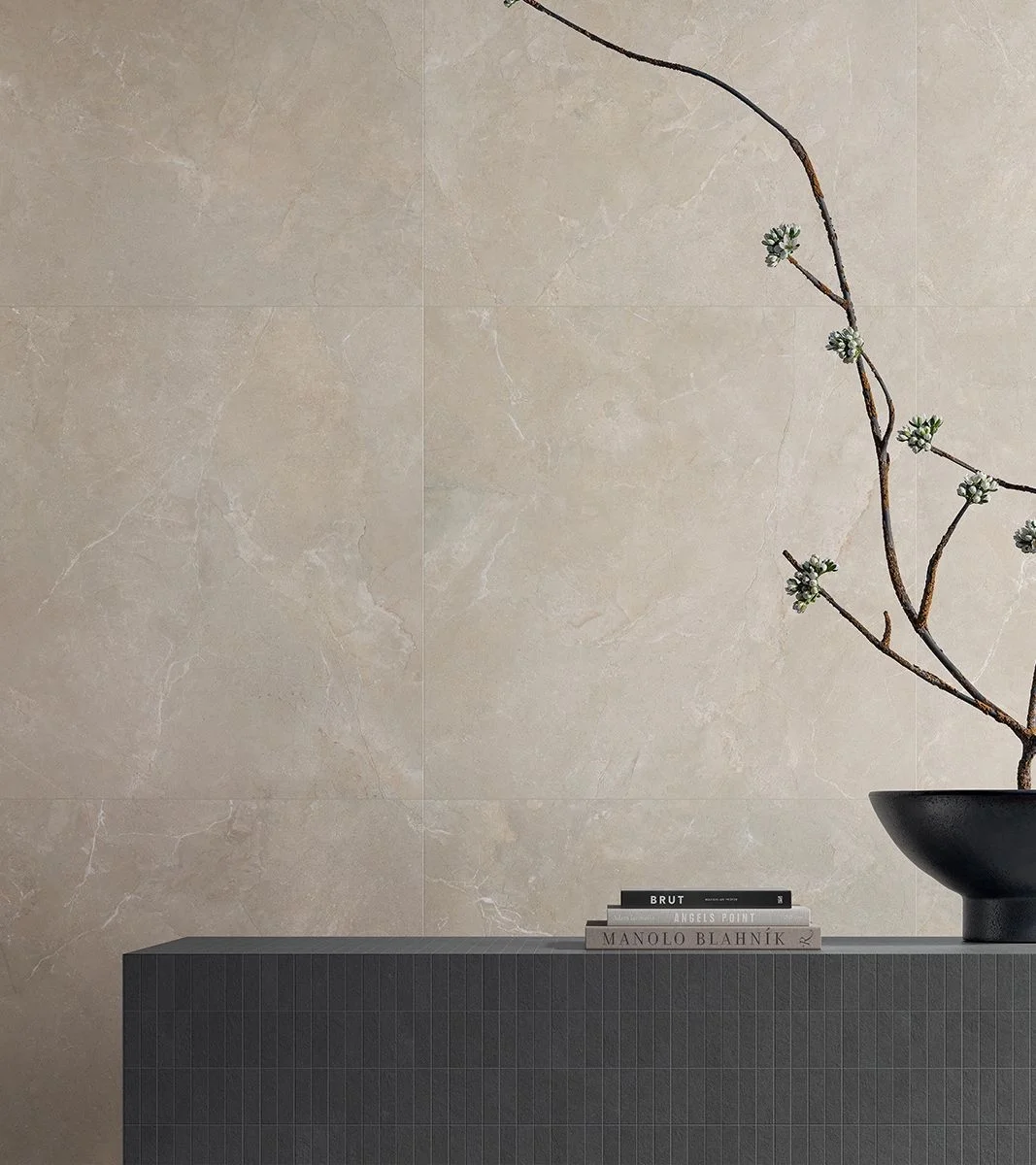 Refined interior wall featuring Arcadia Beige porcelain tile by Italgraniti Group, styled with a modern ribbed vanity, stacked coffee table books, and an arching decorative branch, supplied by PietraCasa.