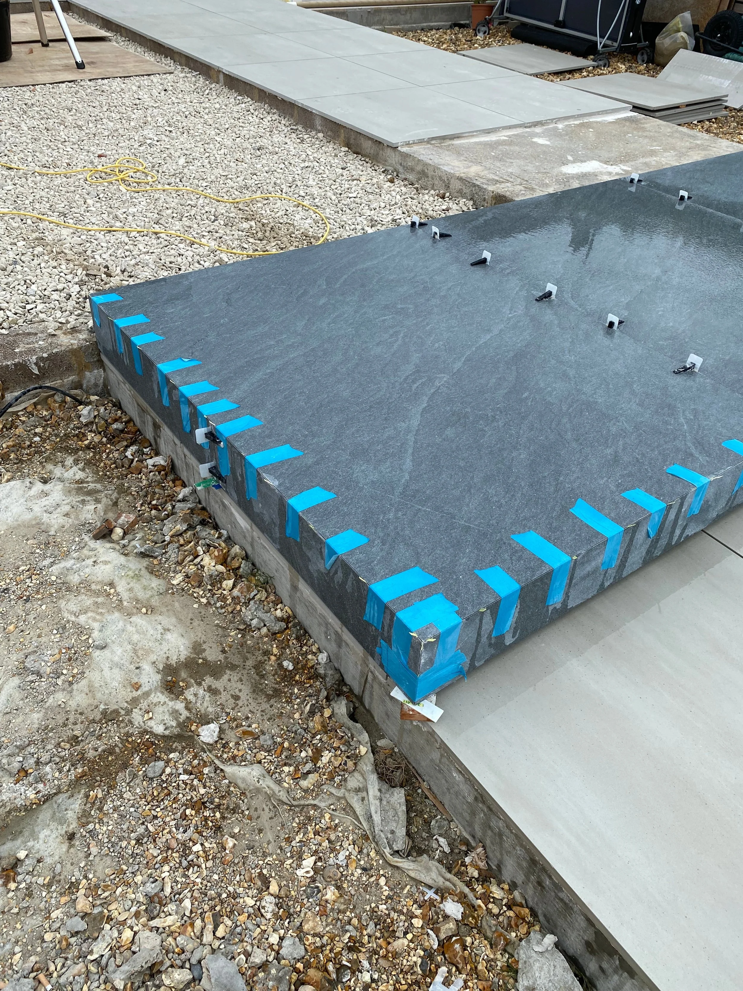 Bespoke outdoor steps clad in textured dark grey porcelain slabs with precision-mitred edges taped during installation.