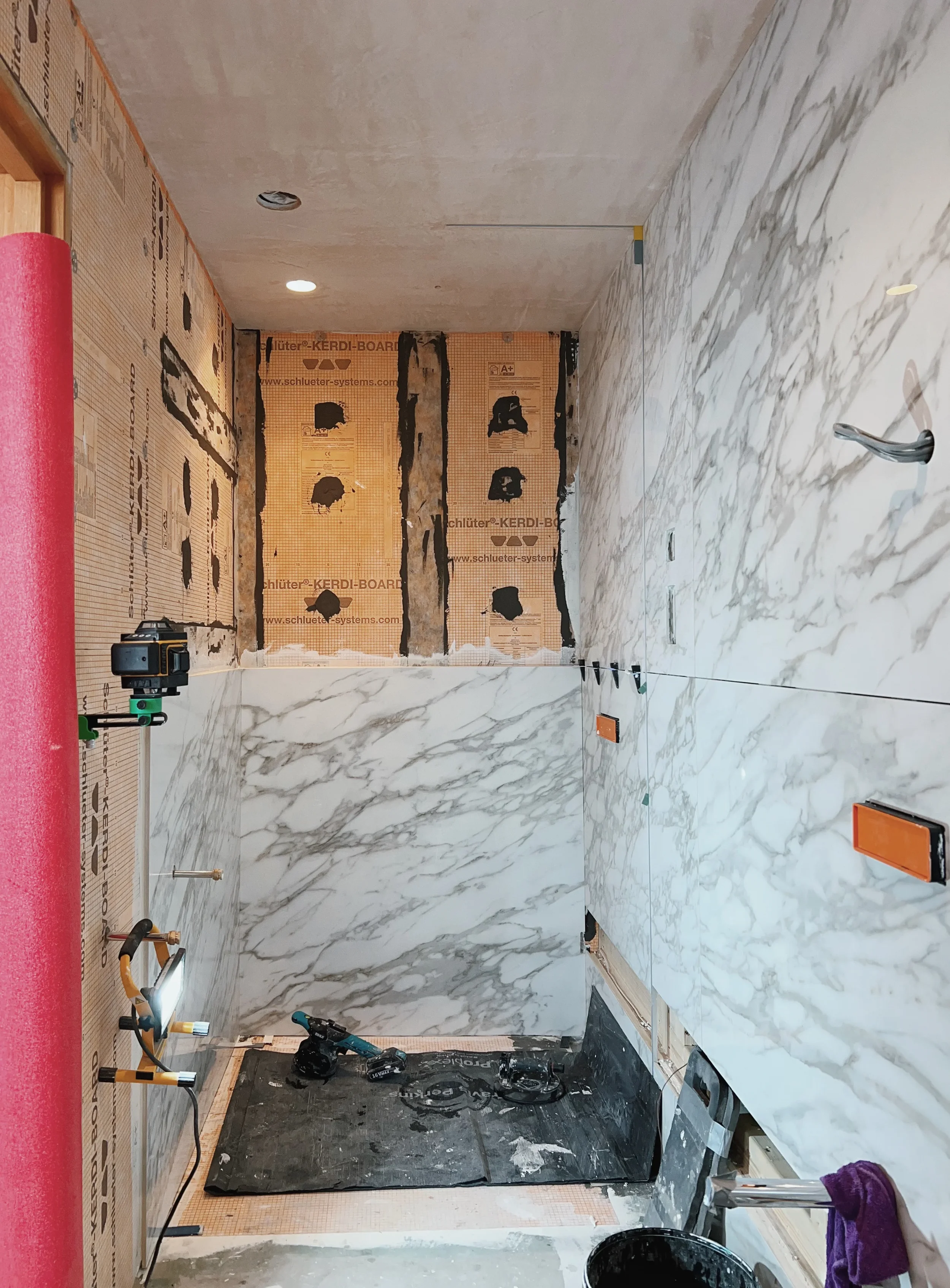 Large-format marble-effect porcelain slabs being installed in a wet room with a laser level.