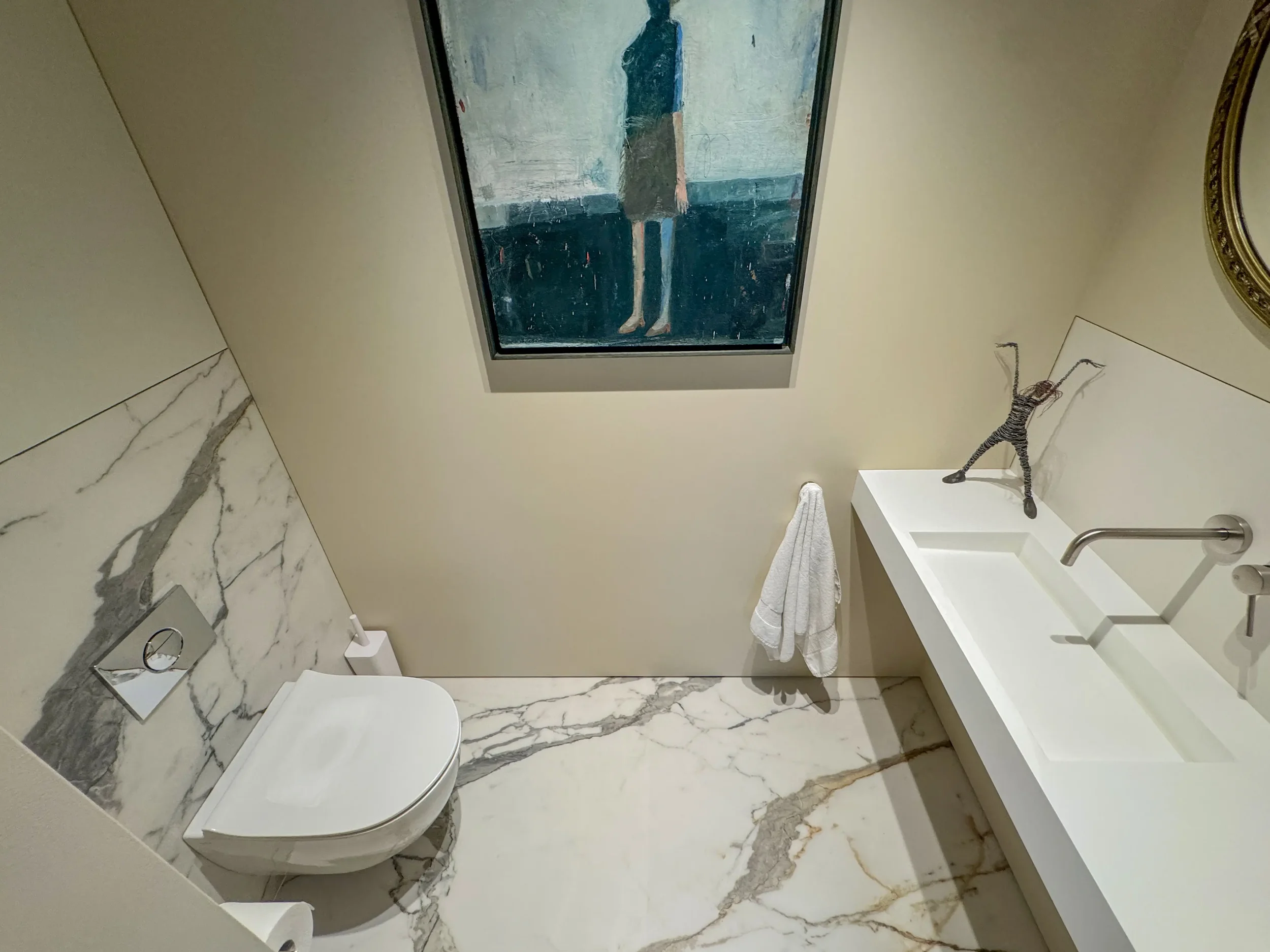 Contemporary cloakroom designed and supplied by Pietracasa and Abitalia, featuring a white Lusso Aura wall-hung stone basin against premium Florim marble-effect porcelain floor and wall tiles, a wall-mounted toilet, and architectural art.