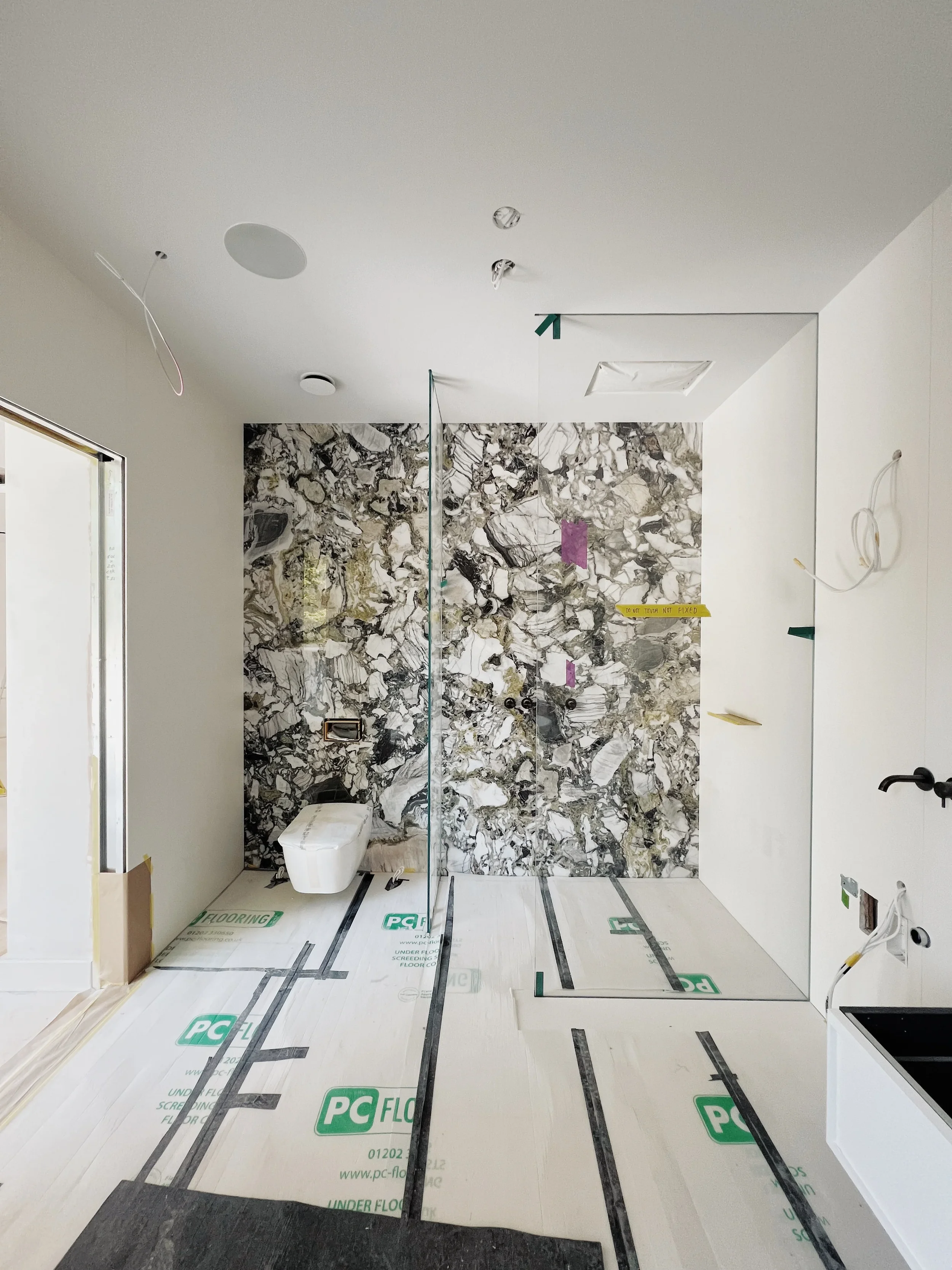 A high-end interior renovation showcasing a dramatic, large-format grey marble-effect porcelain feature wall, currently under installation with leveling clips visible.