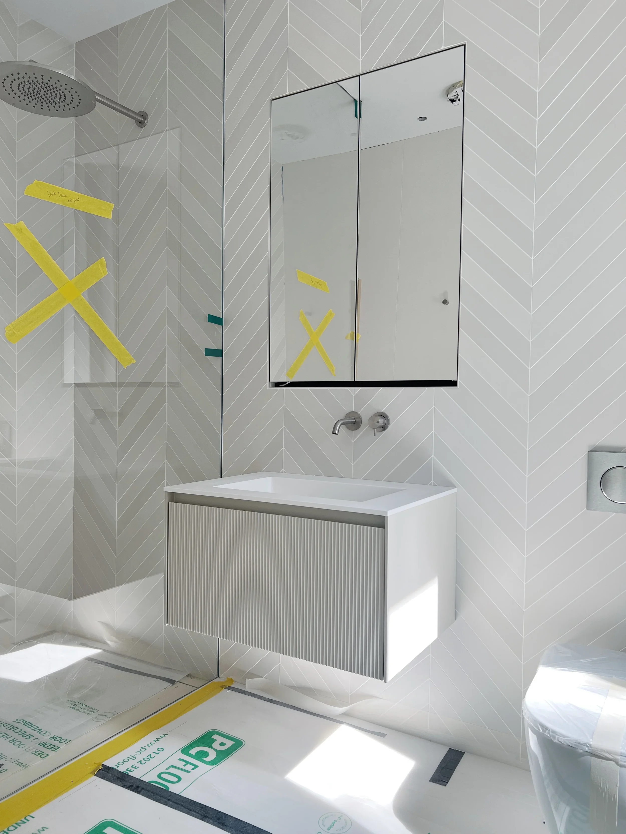 A luxury contemporary bathroom installation featuring a light grey Novello floating vanity unit with a fluted textured drawer front, set against modern white chevron-patterned Mutina wall tiles.