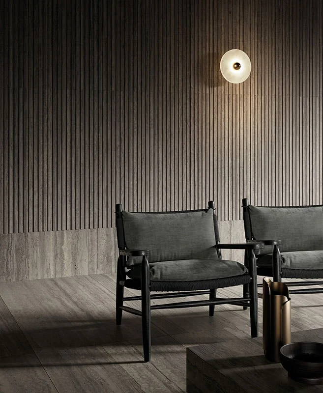 A sophisticated space featuring Kronos Ceramiche's Nativa collection in Lapillo Vena, including Minibaguette 3D wall textures, paired with Flexform’s Tessa lounge chairs by Antonio Citterio, available through PietraCasa.