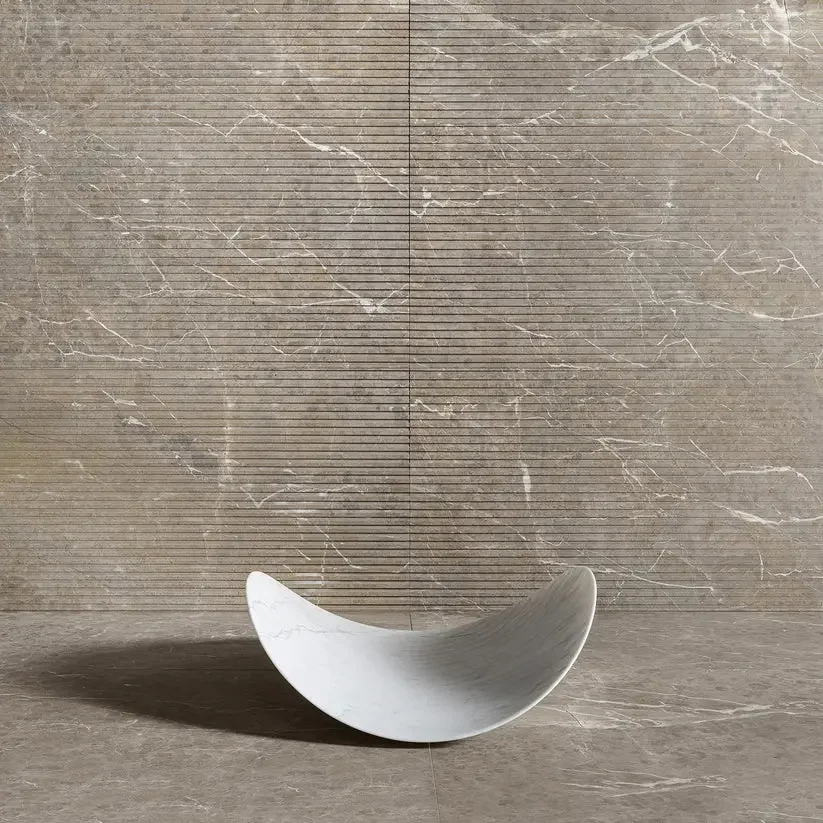 A sleek, crescent-shaped marble basin from the Luce di Carrara collection, designed by Attila Veress, showcased against textured, fluted marble wall panels and flooring, available through PietraCasa.