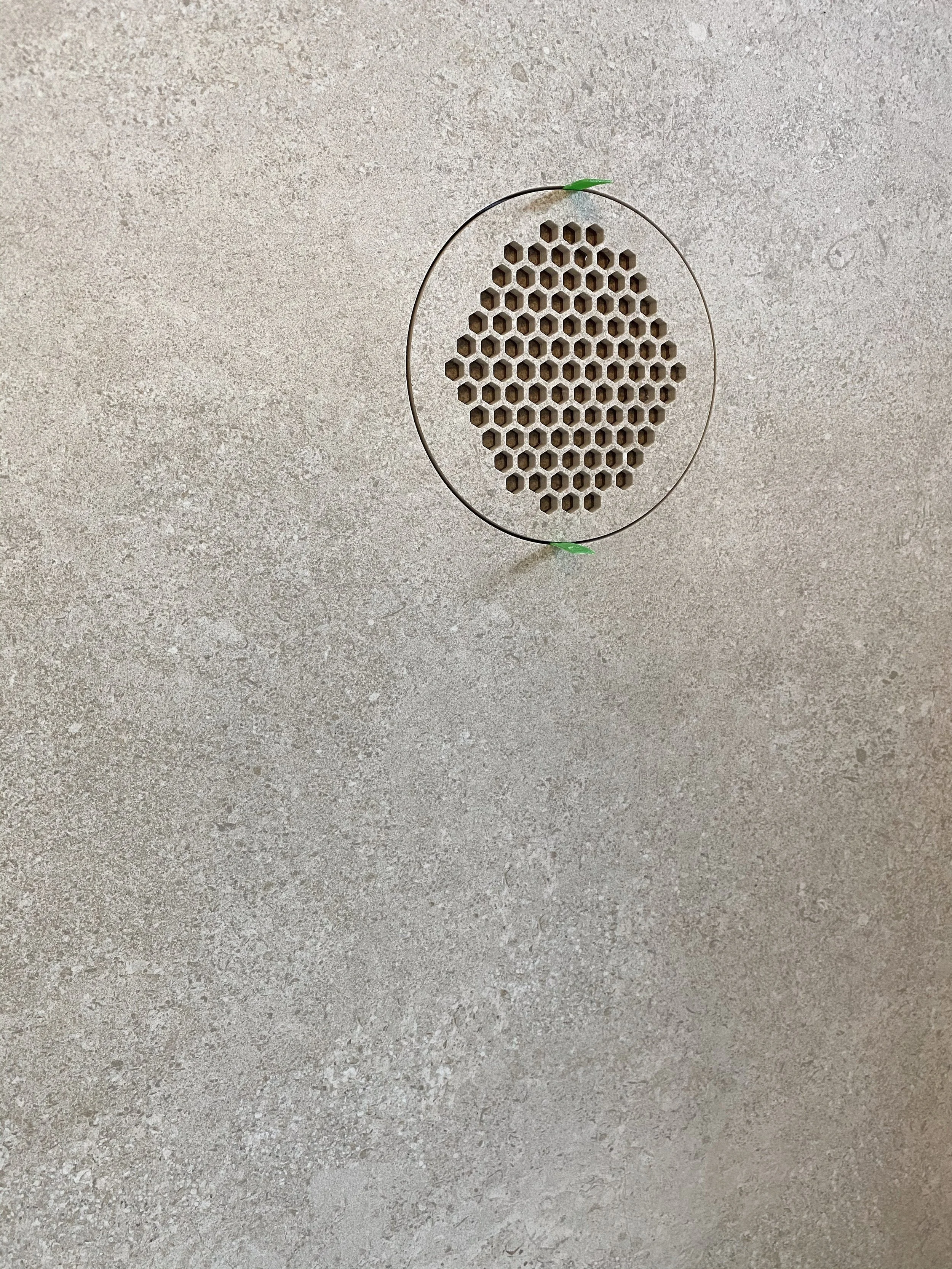 Custom waterjet cut circular floor drain featuring an intricate hexagonal honeycomb grate pattern fabricated into stone-effect porcelain tile by PietraCasa.