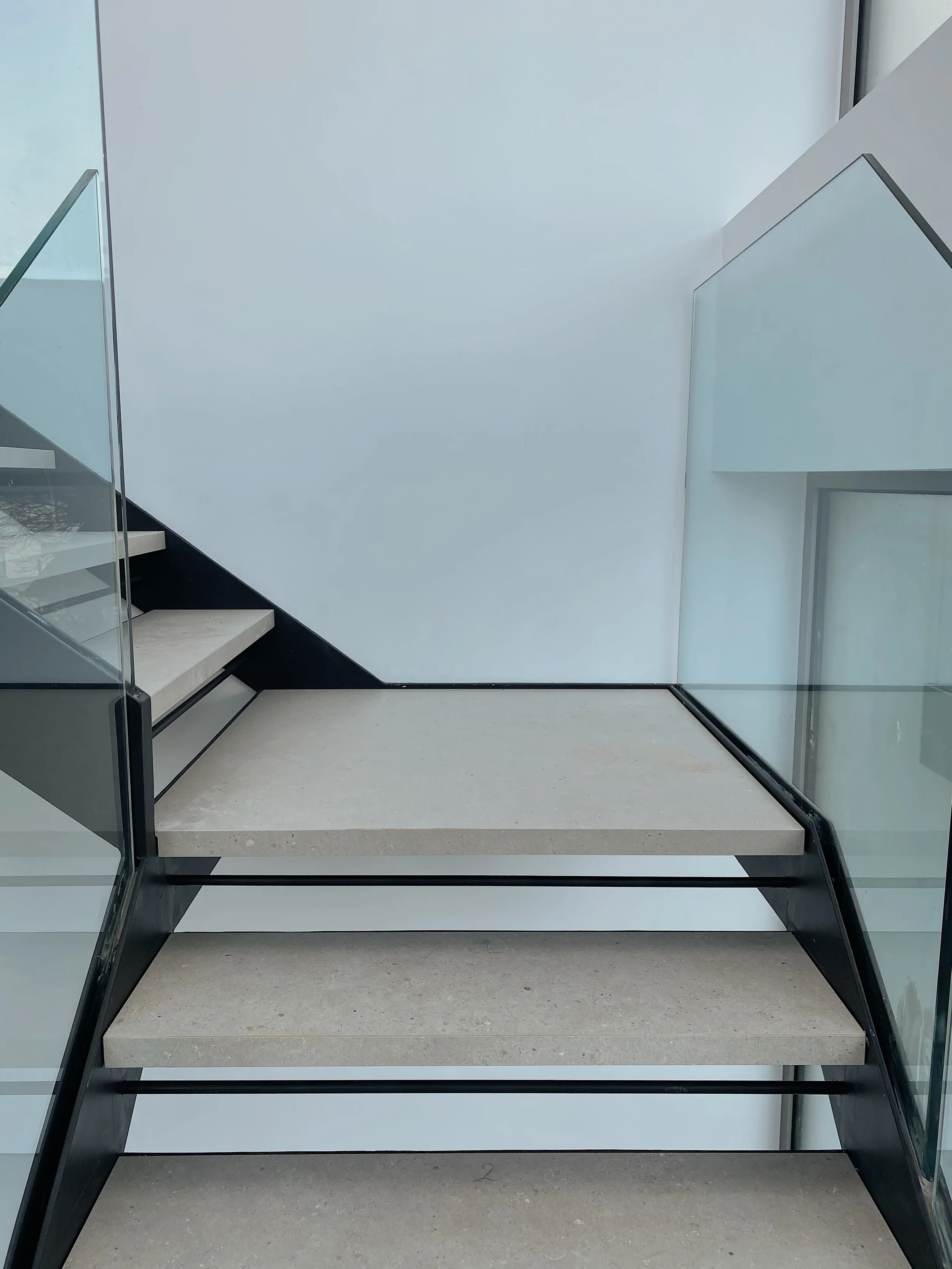 Contemporary cantilevered staircase design showcasing premium large-format porcelain cladding on steps and landing platforms with minimalist glass guarding in a luxury interior.