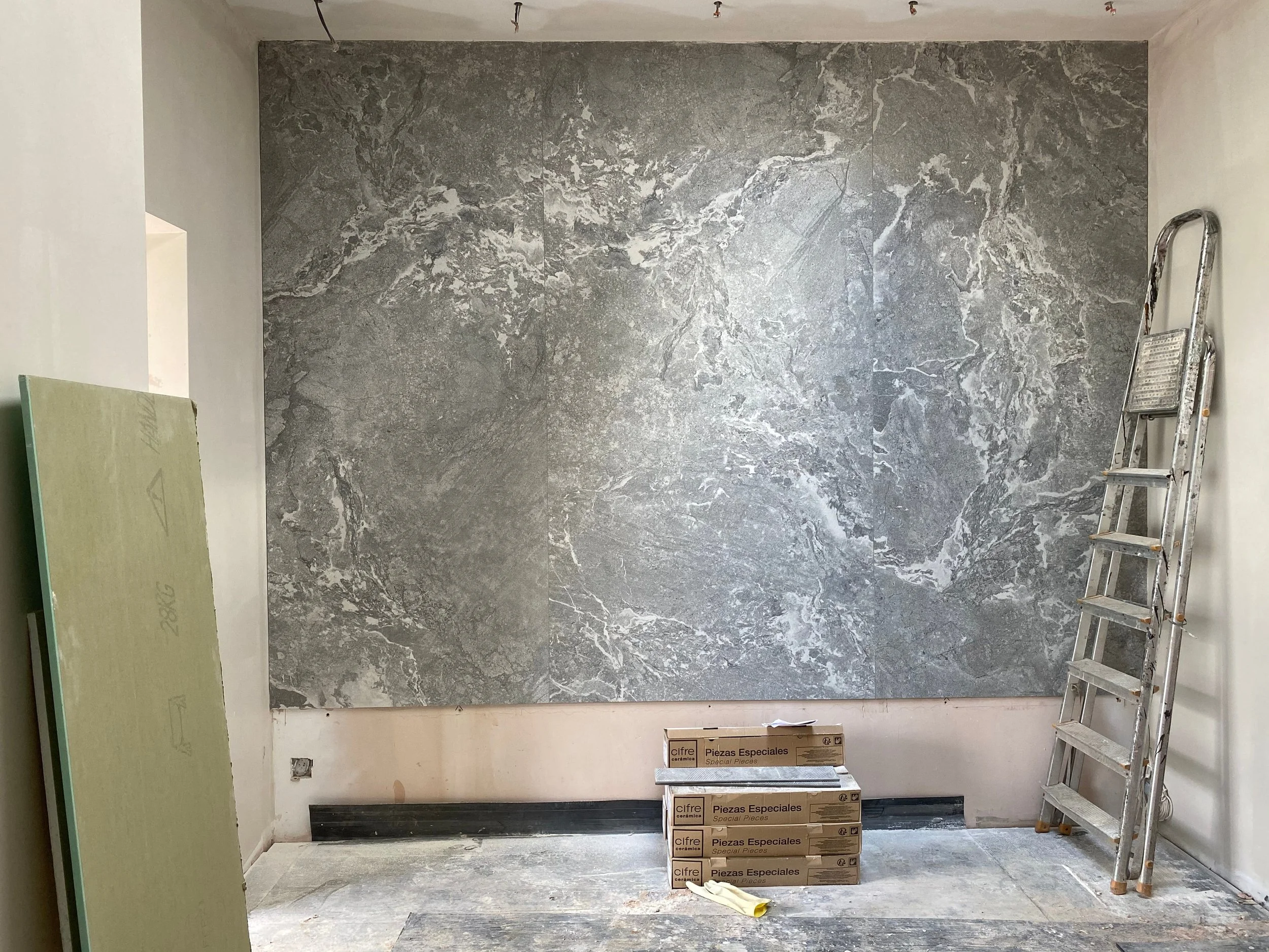 A high-end interior renovation under construction, featuring a striking, large-format grey marble-effect porcelain feature wall with complex veining that serves as a bold design statement.