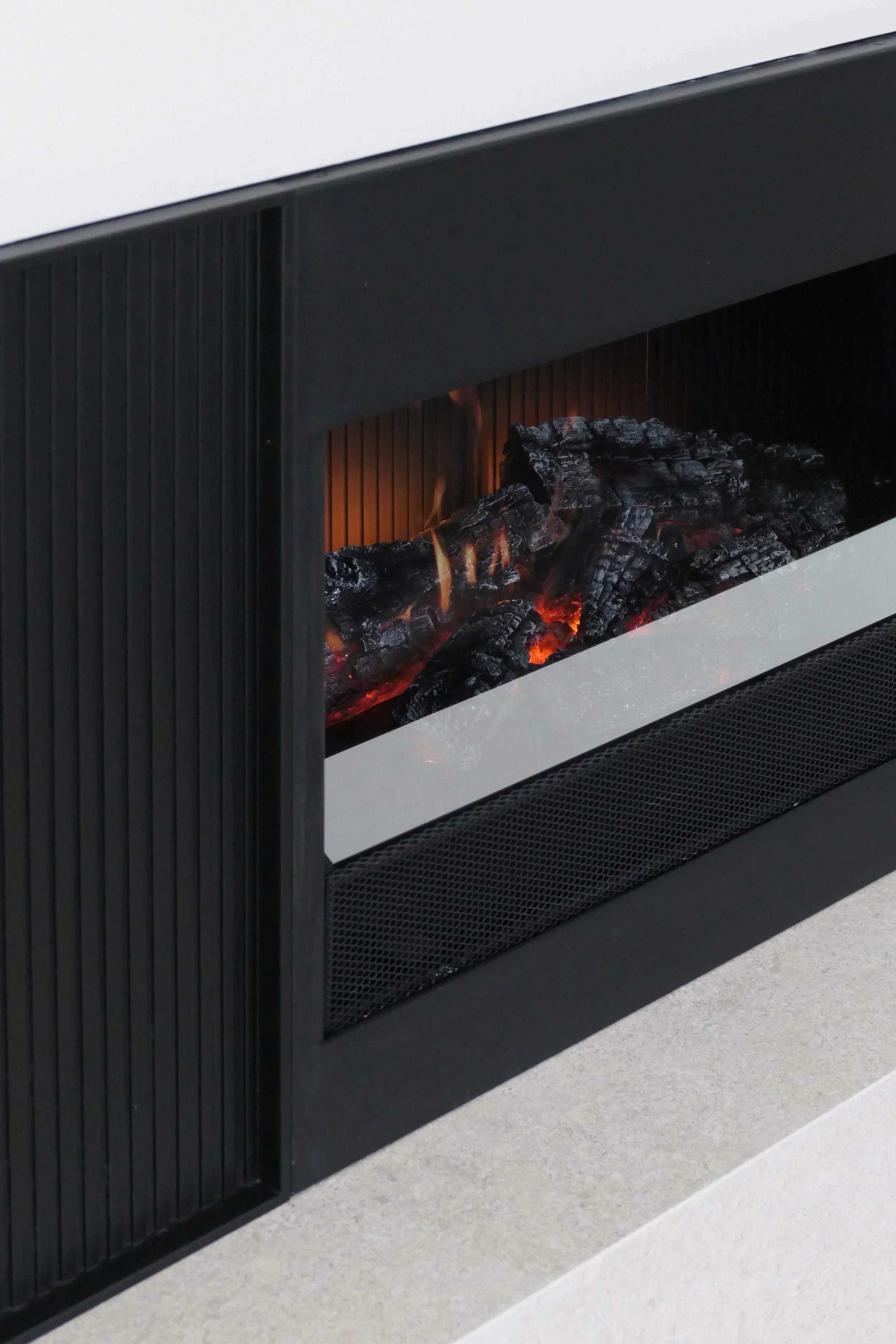 Close-up view of a luxury contemporary inset electric fireplace featuring realistic glowing log media and an integrated flame effect, flanked by matte black fluted accent panels.