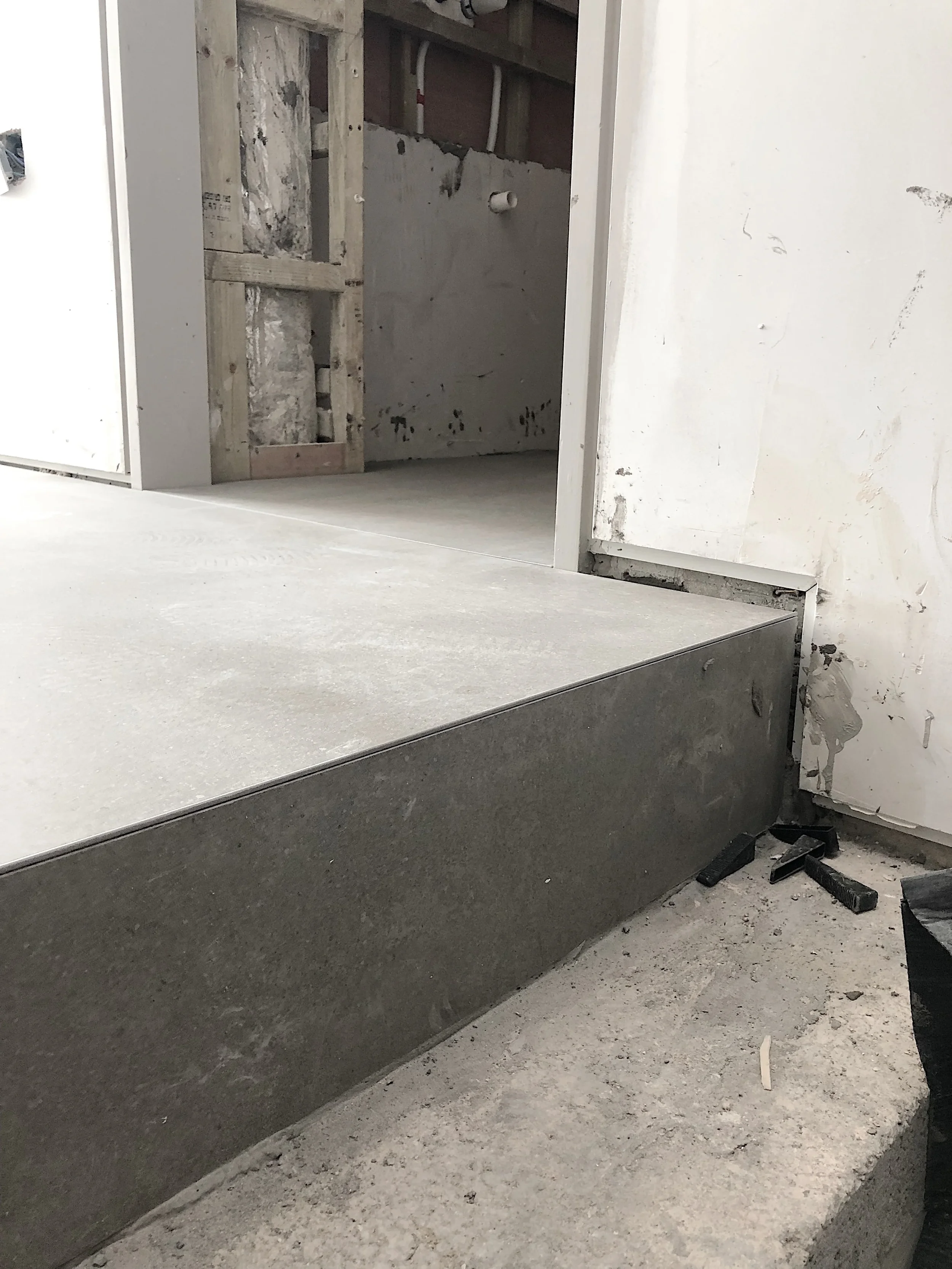 Close-up of a large-format porcelain step detail under construction, highlighting a sleek, minimalist profile edge achieved using a Schlüter-FINEC tile trim over grey concrete-effect porcelain slabs.