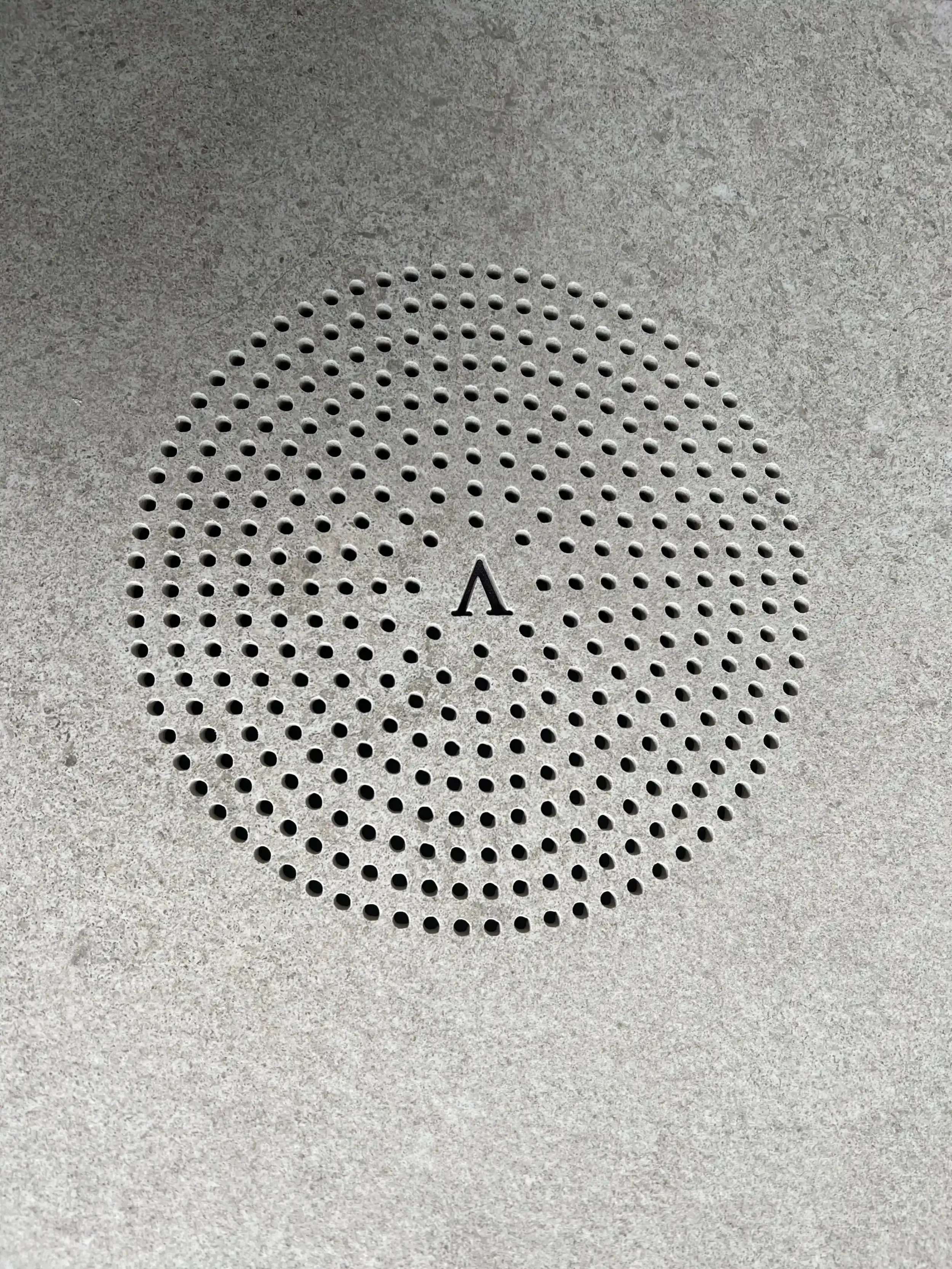 PietraCasa brand logo and stylized 'A' icon precision engraved into the center of a custom waterjet cut micro-perforated circular porcelain floor drain.