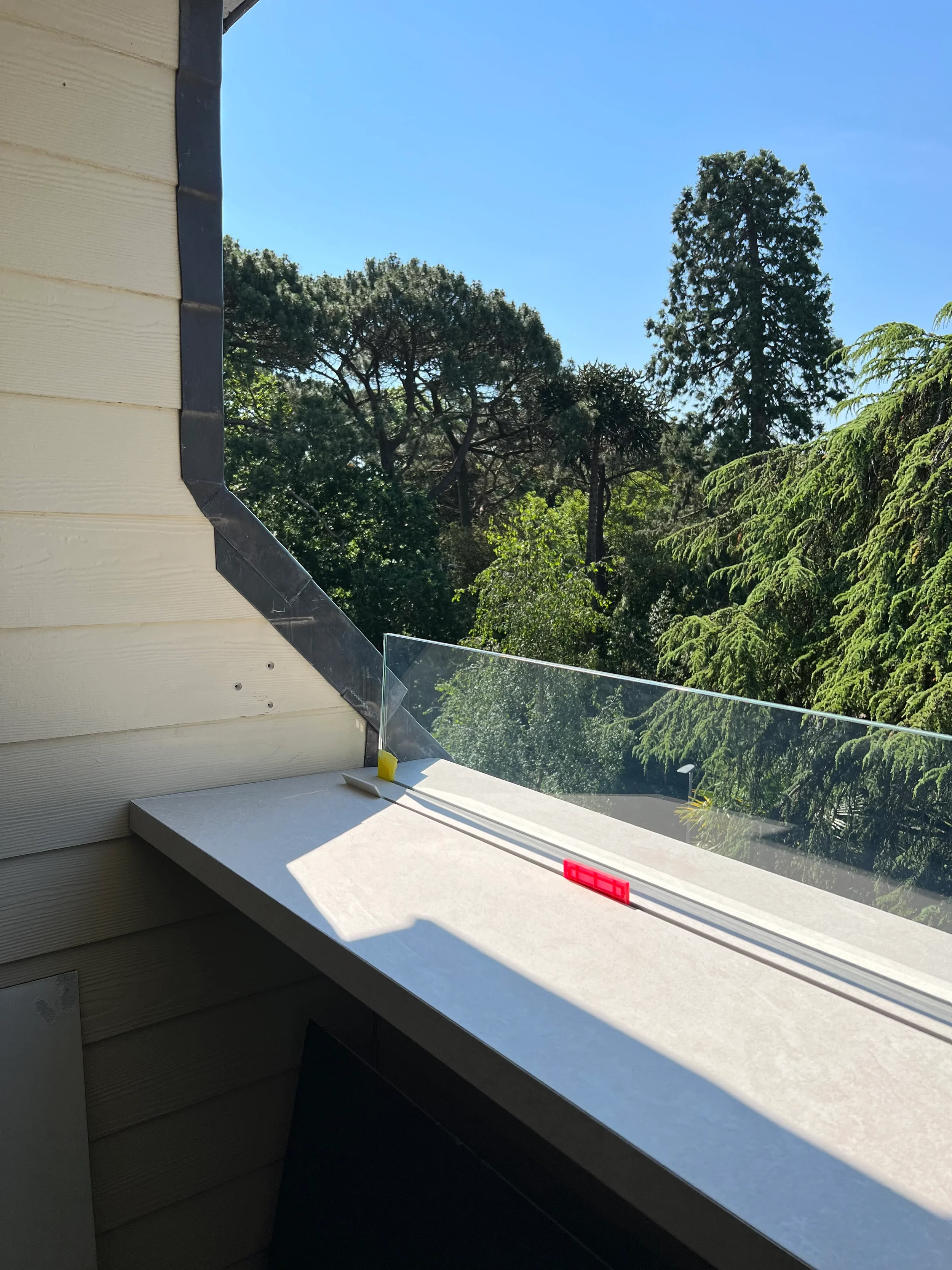 recision-cut outdoor porcelain slab coping being installed on a modern balcony overlooking trees during construction.