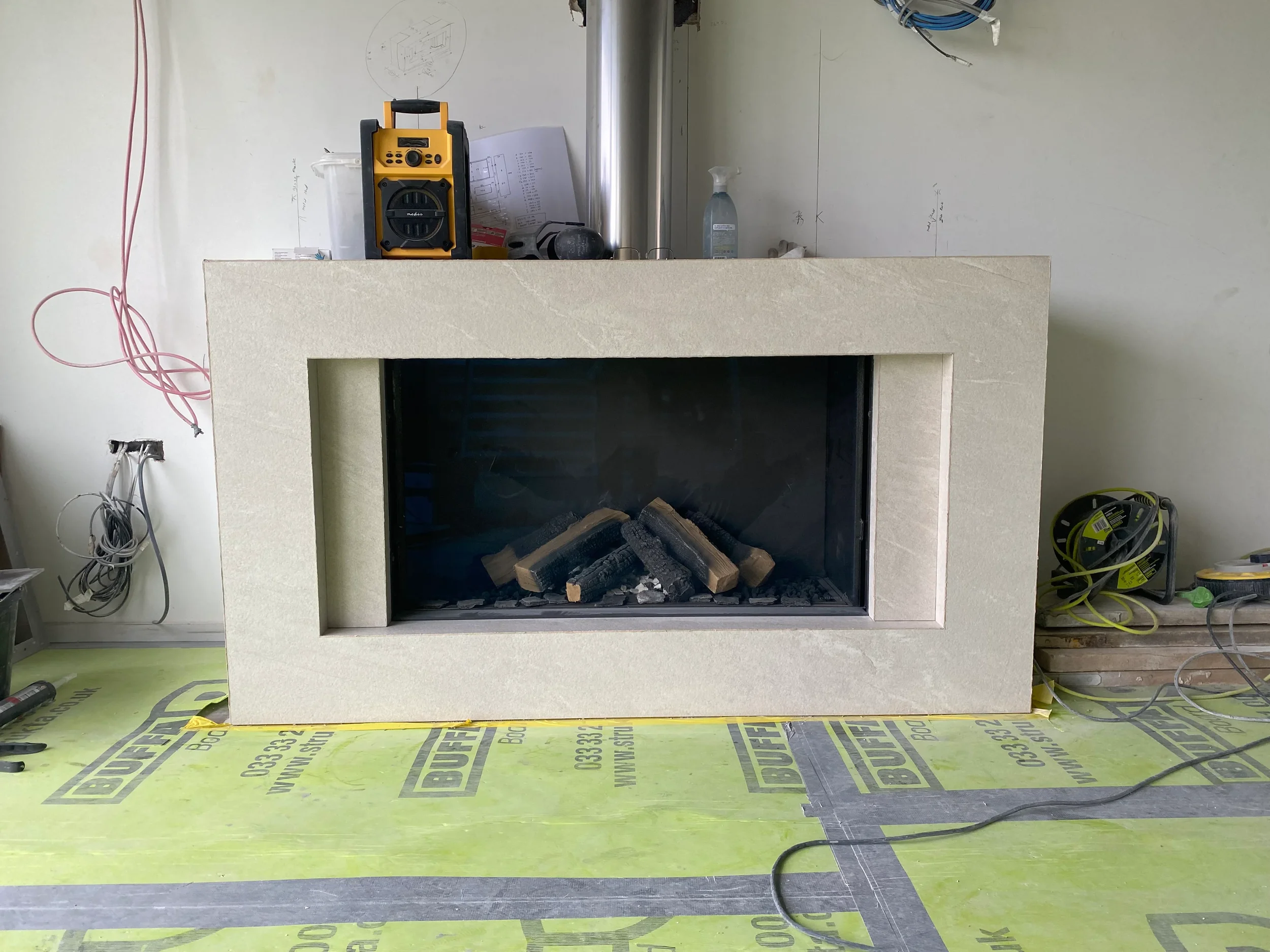 A luxury contemporary fireplace surround custom-fabricated from textured cream stone-effect porcelain slabs with precise mitred joints.