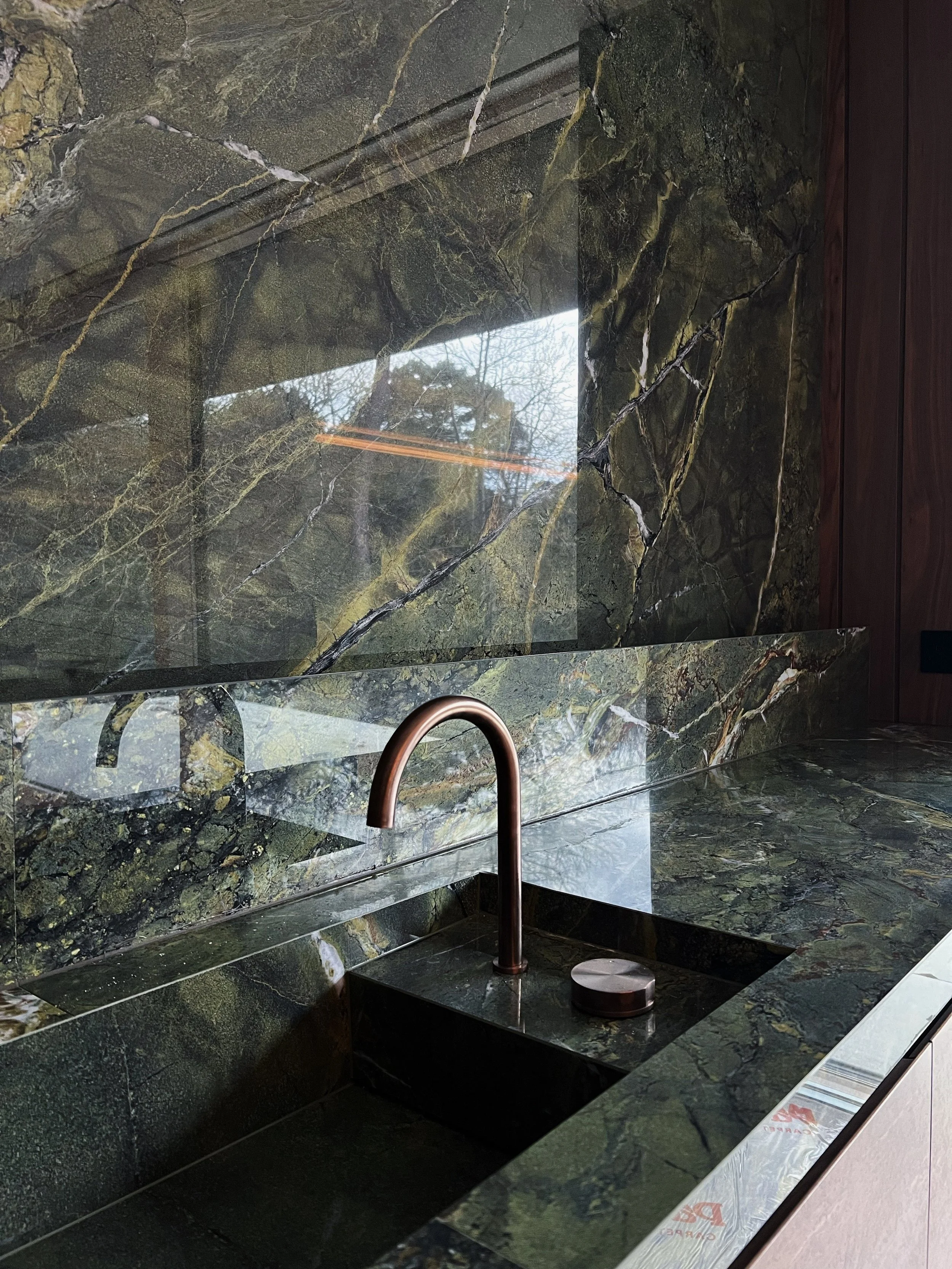 A high-end kitchen design featuring a stunning, seamless green marble-effect porcelain surface and integrated sink, complemented by a sophisticated copper faucet.