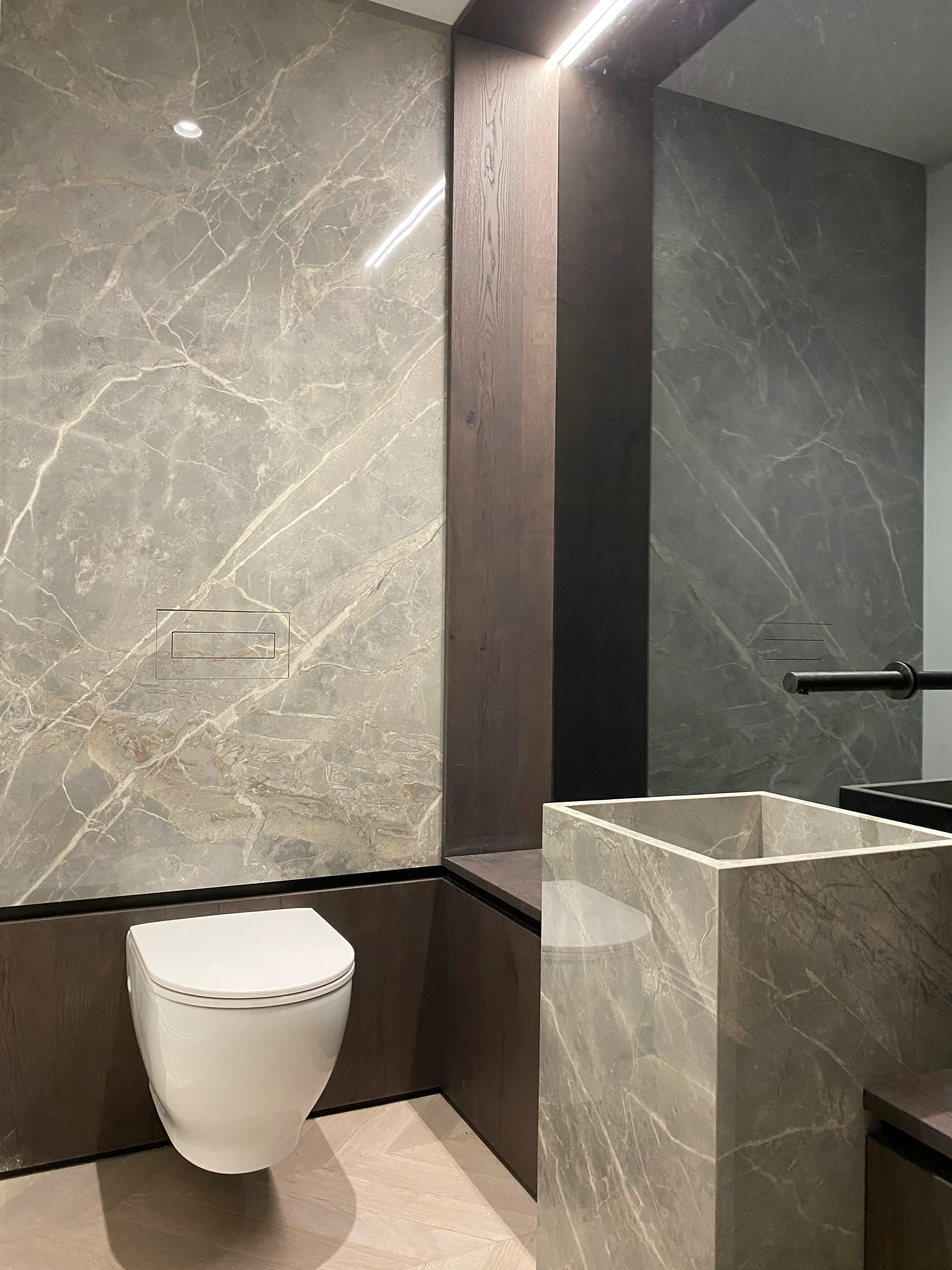 A luxury contemporary cloakroom featuring a custom fabricated monolithic totem basin and matching large-format grey marble-effect porcelain wall panels by PietraCasa.
