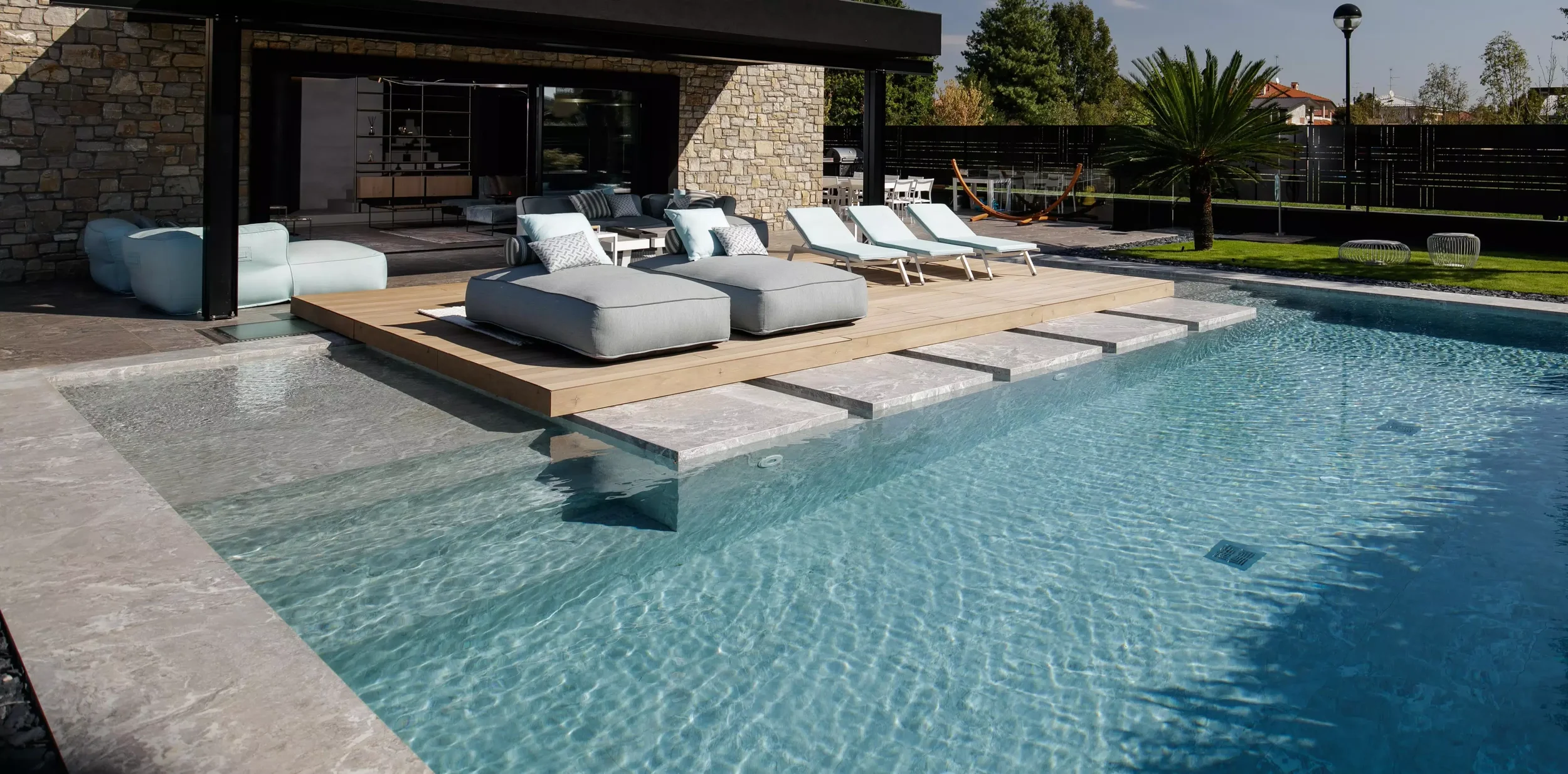Modern outdoor patio and swimming pool design featuring light-colored stone-effect porcelain stoneware tiles from the Florim Onyx&More collection, expertly supplied and installed by PietraCasa.