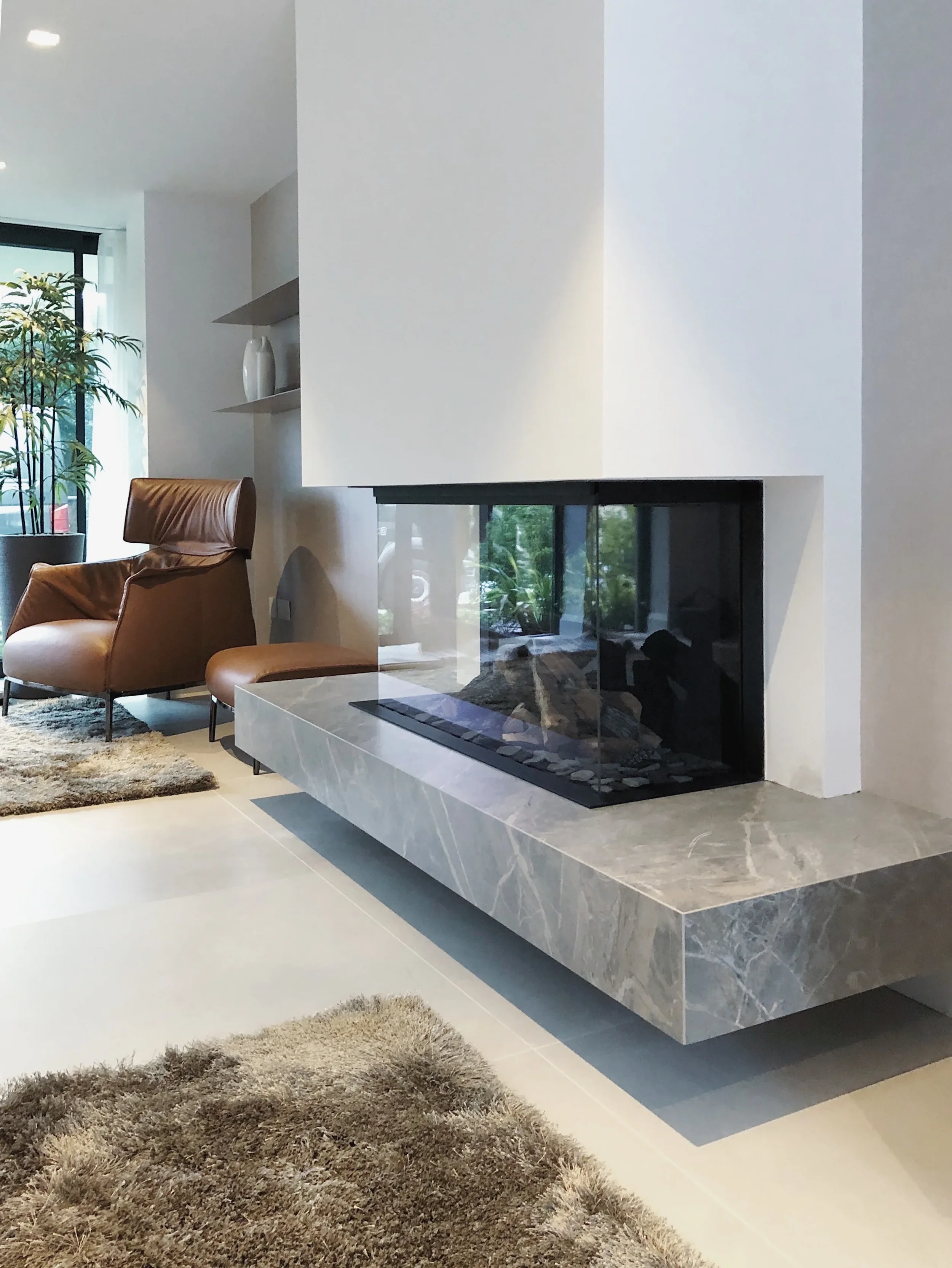 A luxury modern living room showcase featuring a low-profile cantilevered floating hearth custom-fabricated from grey marble-effect porcelain slabs, integrated with a contemporary three-sided glass fireplace.