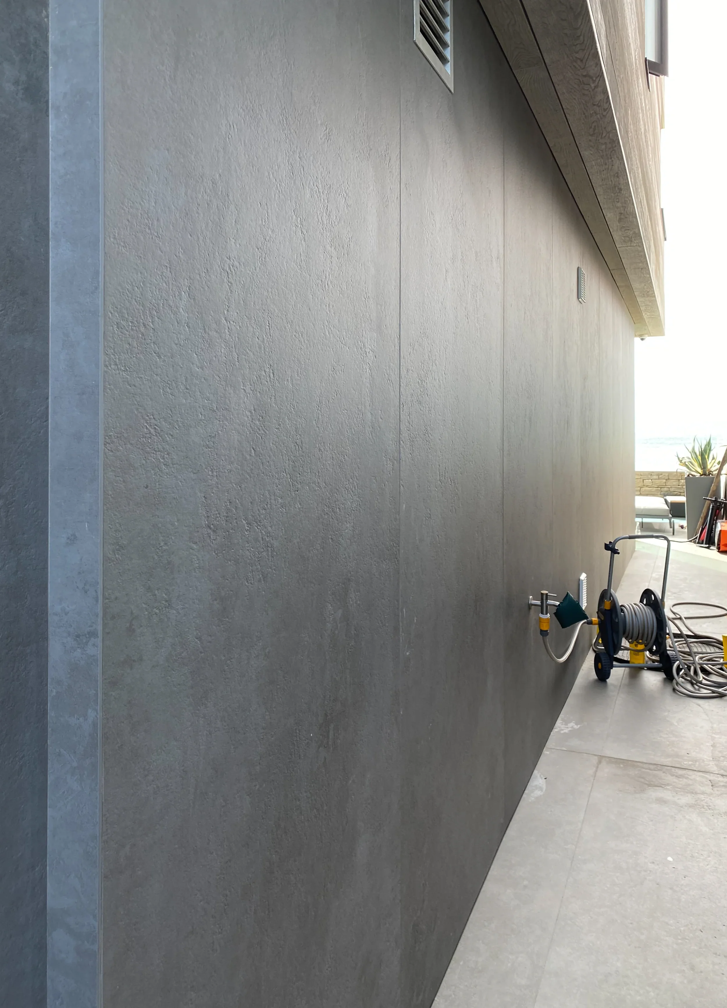 A contemporary outdoor space featuring seamless, large-format grey porcelain wall cladding that creates a clean, minimalist architectural facade.