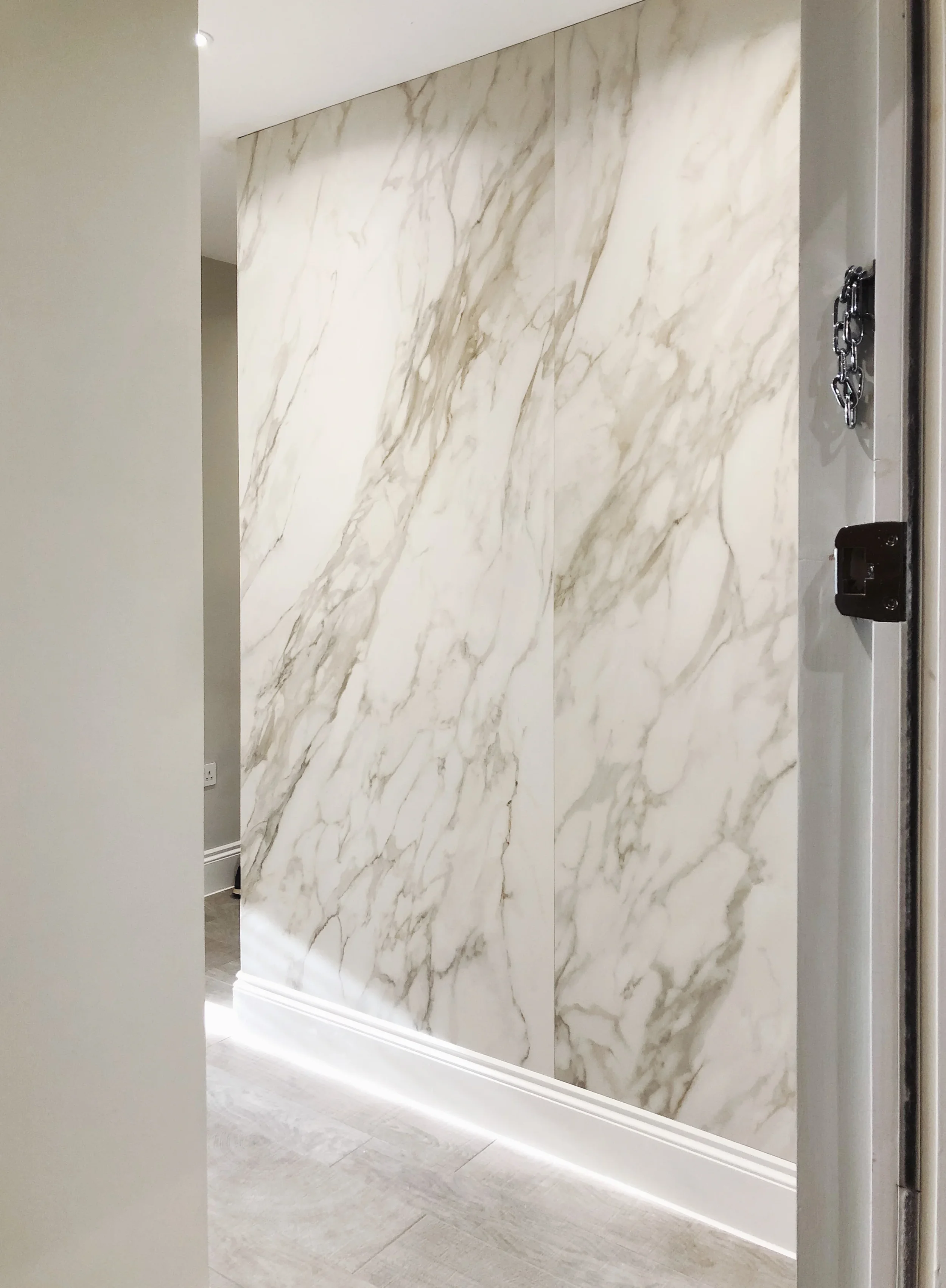 A high-end residential interior featuring a dramatic, seamless large-format marble-effect porcelain feature wall, demonstrating sophisticated architectural application.