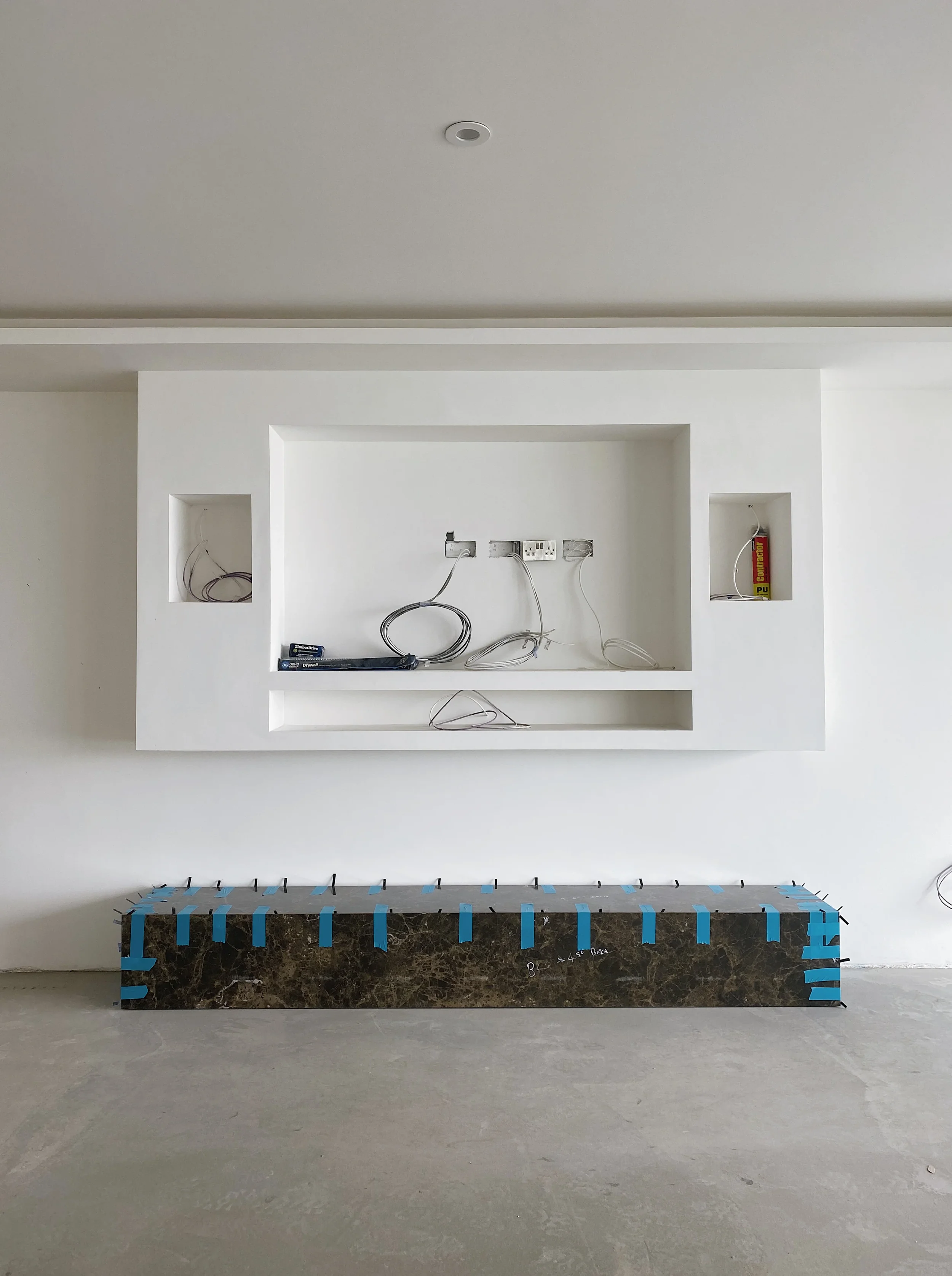 A high-end, contemporary media wall under construction, featuring a dramatic, dark marble-effect porcelain hearth contrasted against a crisp, white minimalist framework.