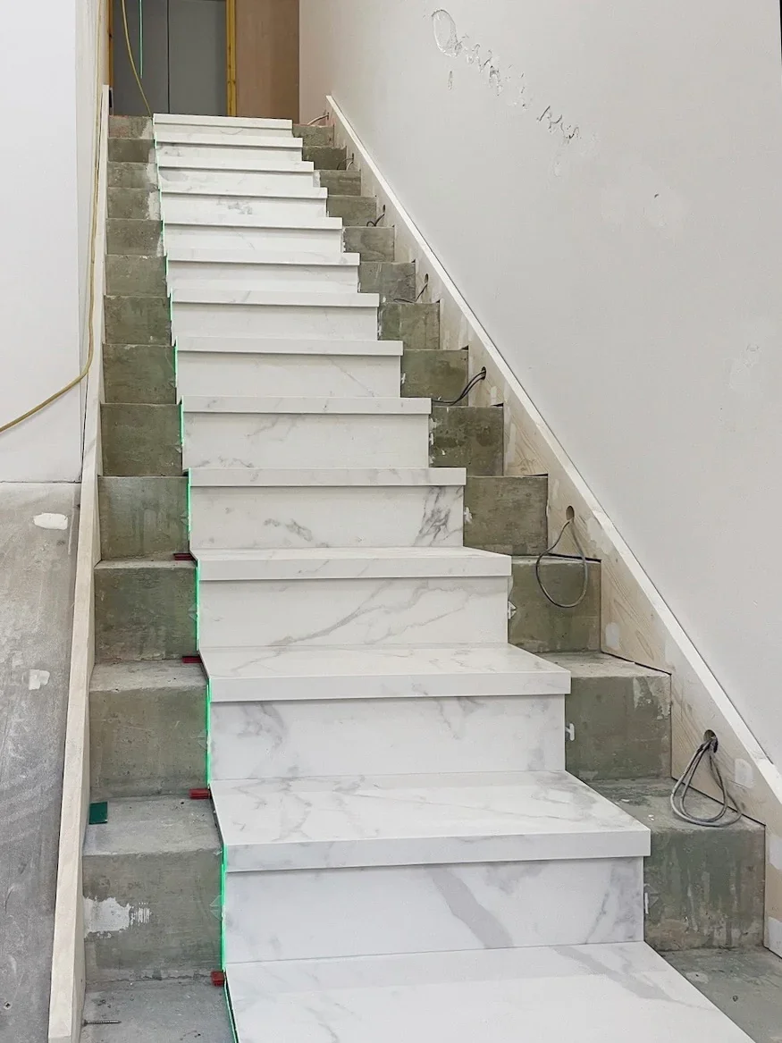 A luxury contemporary internal staircase featuring custom-fabricated steps clad in large-format marble-effect white porcelain slabs with precision-mitred drop-front treads under construction.