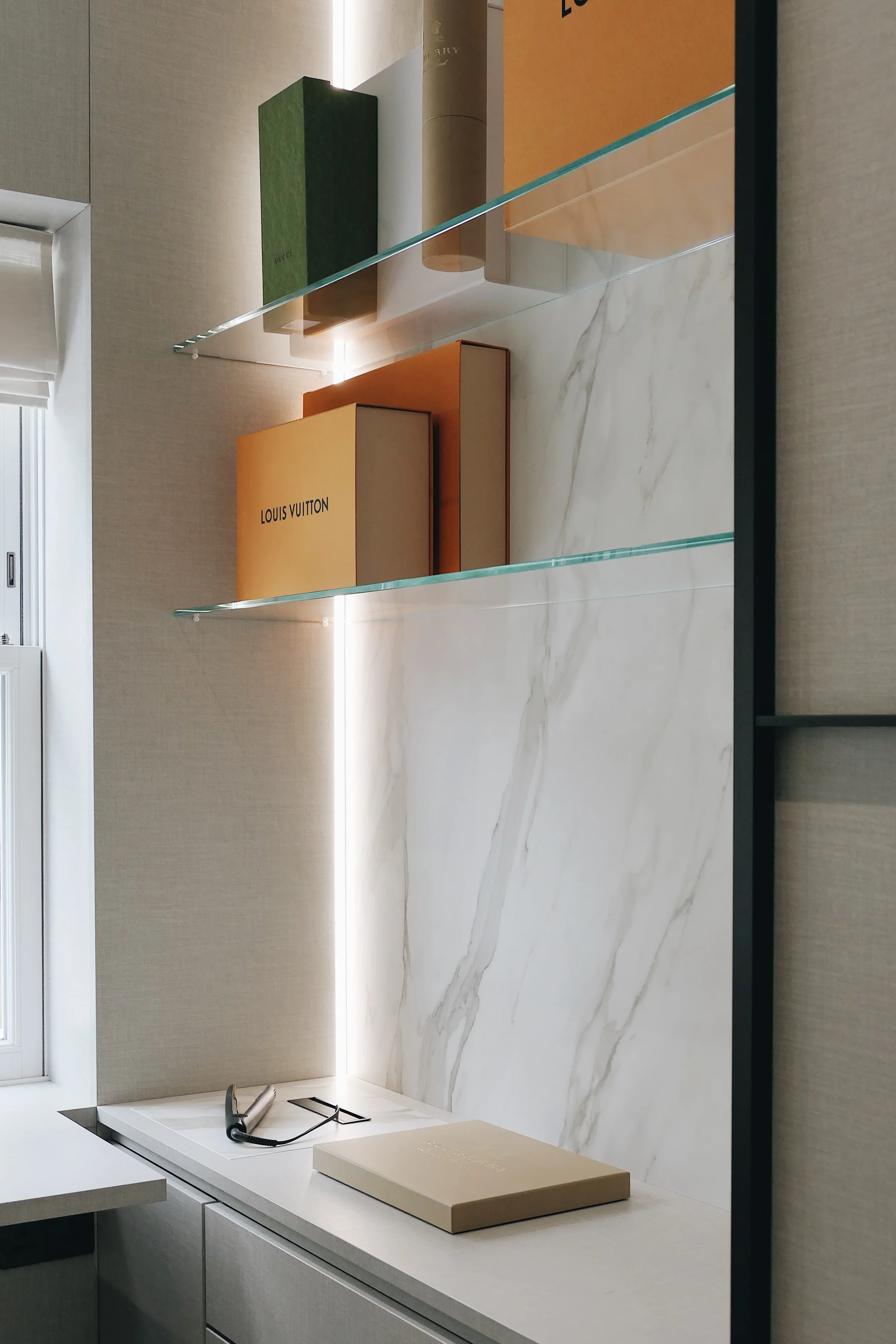 A high-end interior detail showcasing custom glass shelving set against a seamless, large-format marble-effect porcelain backsplash, featuring integrated accent lighting.
