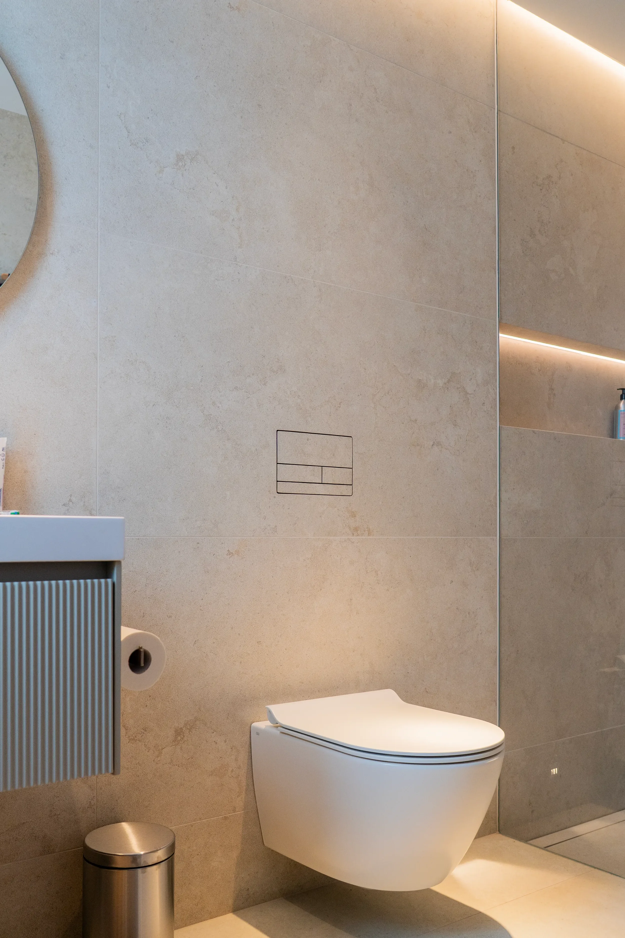 Modern wall-mounted toilet with a Clanea flush plate integrated into premium Living Ceramics Verso Cross Cut Light Arco stone-effect porcelain tile surfaces by Abitalia & Pietracasa.