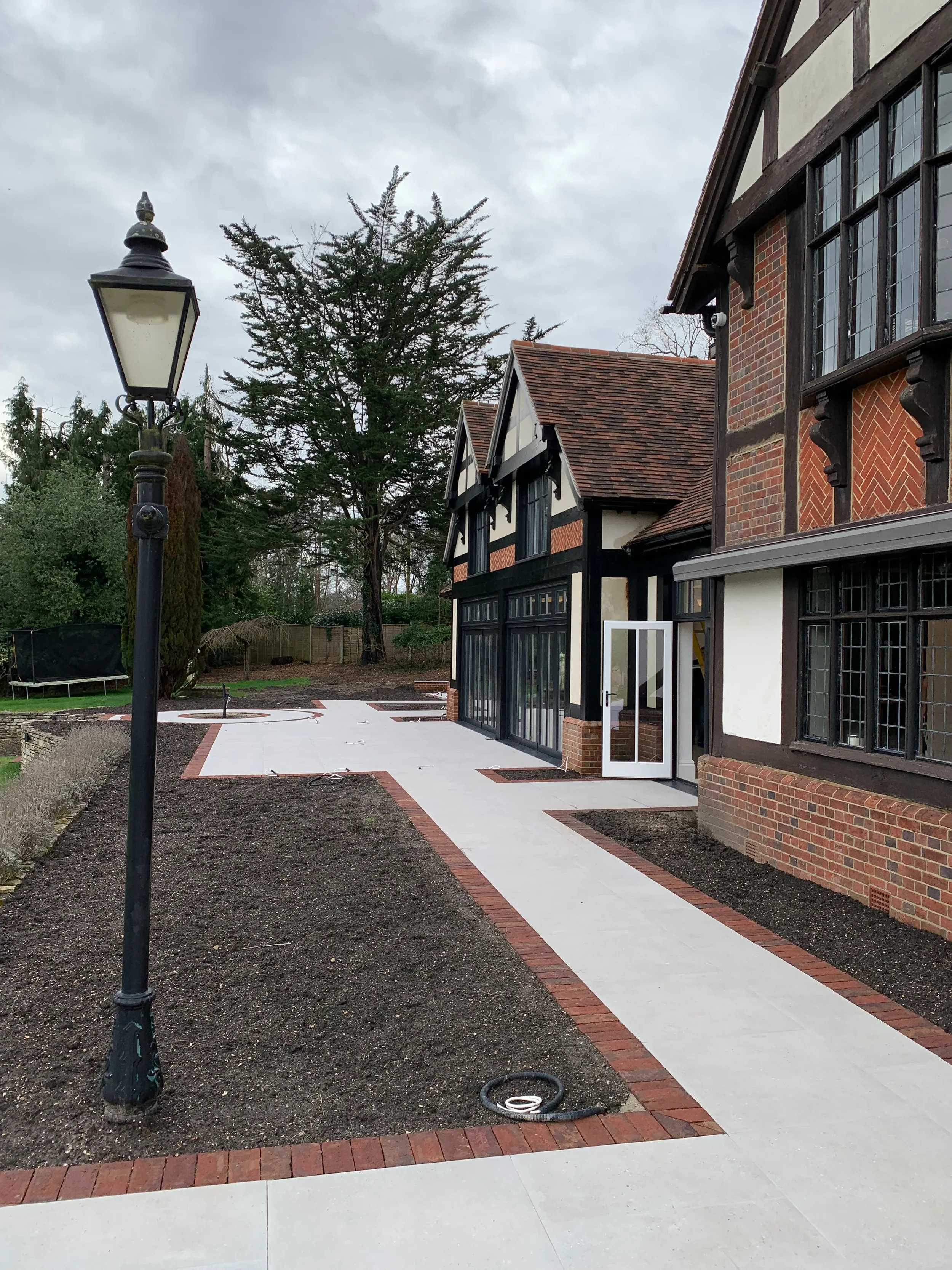 Newly installed external porcelain slab pathways and courtyard patio surrounding a historic timber-framed brick house.
