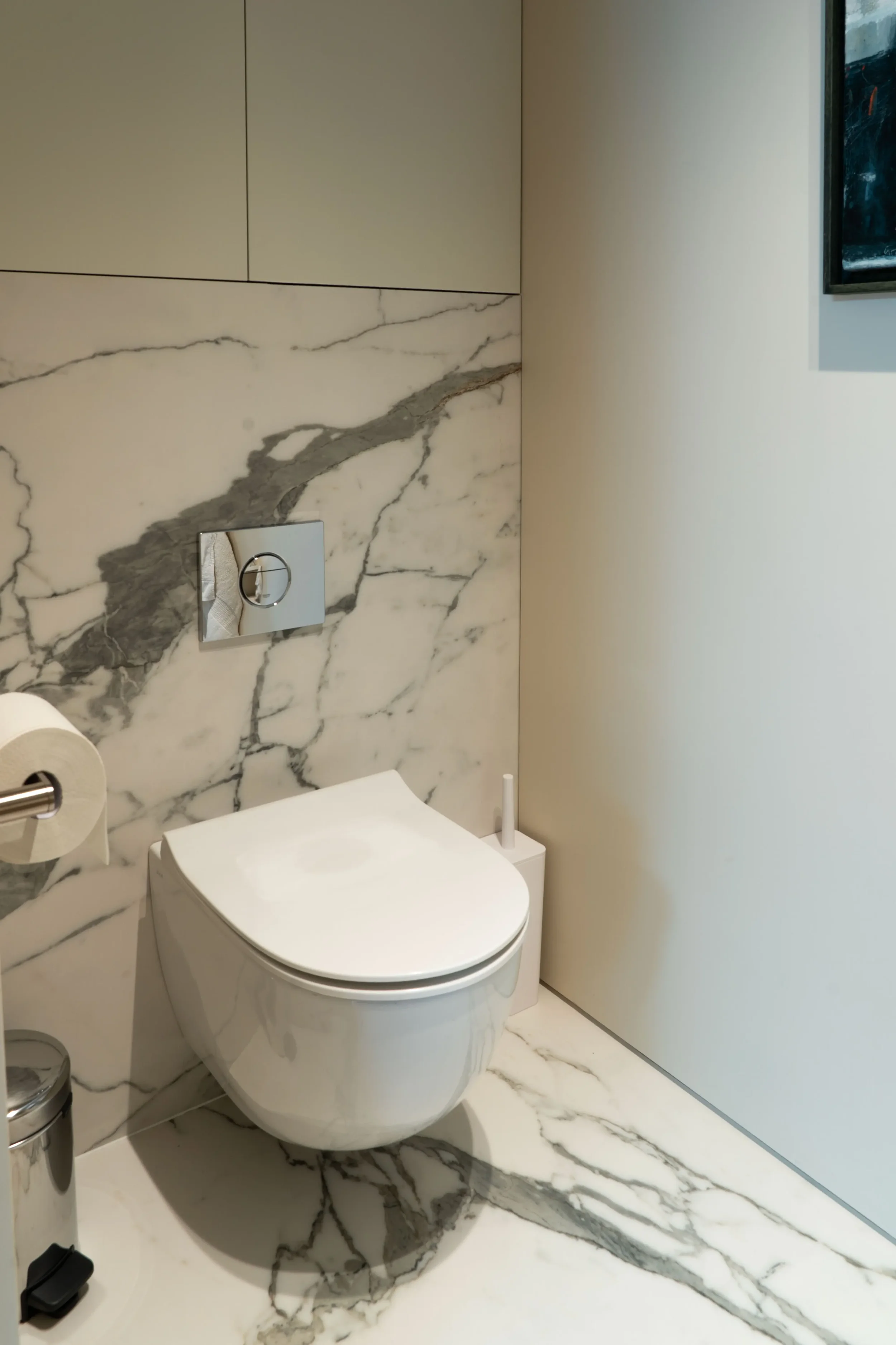 Contemporary cloakroom interior designed and supplied by Pietracasa and Abitalia, featuring a white wall-hung toilet pan with a chrome dual-flush plate, set against premium bookmatched Florim white marble-effect porcelain tiles clad seamlessly on the