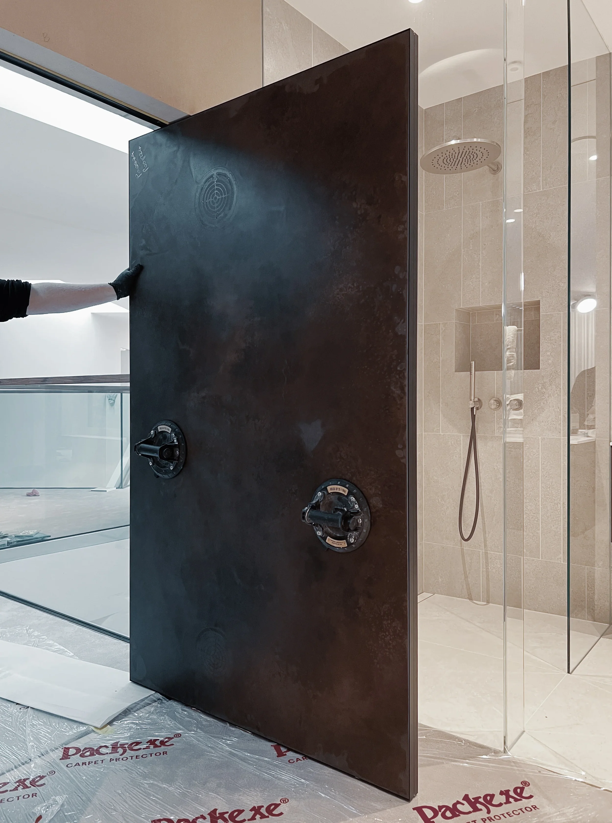 A professional installation shot showcasing the expert handling and precise placement of a bespoke-fabricated, large-format dark porcelain panel, emphasizing meticulous craftsmanship in a luxury bathroom renovation.