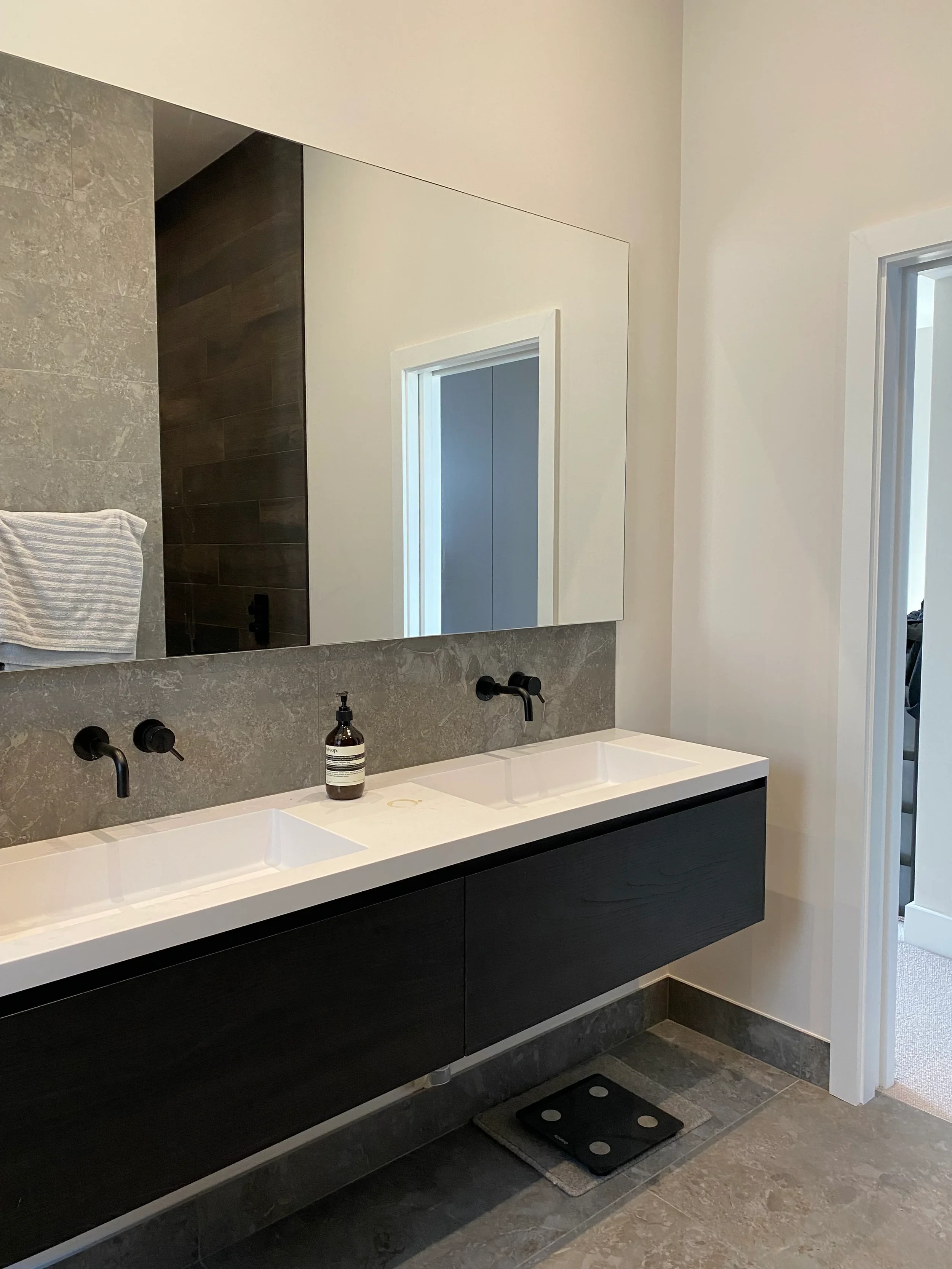 Dark timber floating double vanity and wall-mounted black taps with a grey porcelain tile splashback