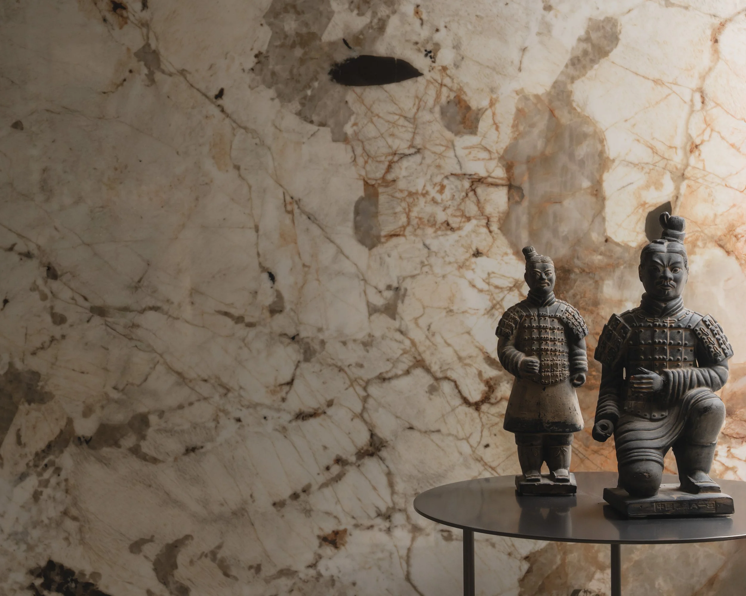 Premium large-format porcelain slab display with a bookmatched stone-effect pattern behind decorative Terracotta Warrior statues at the PietraCasa showroom.