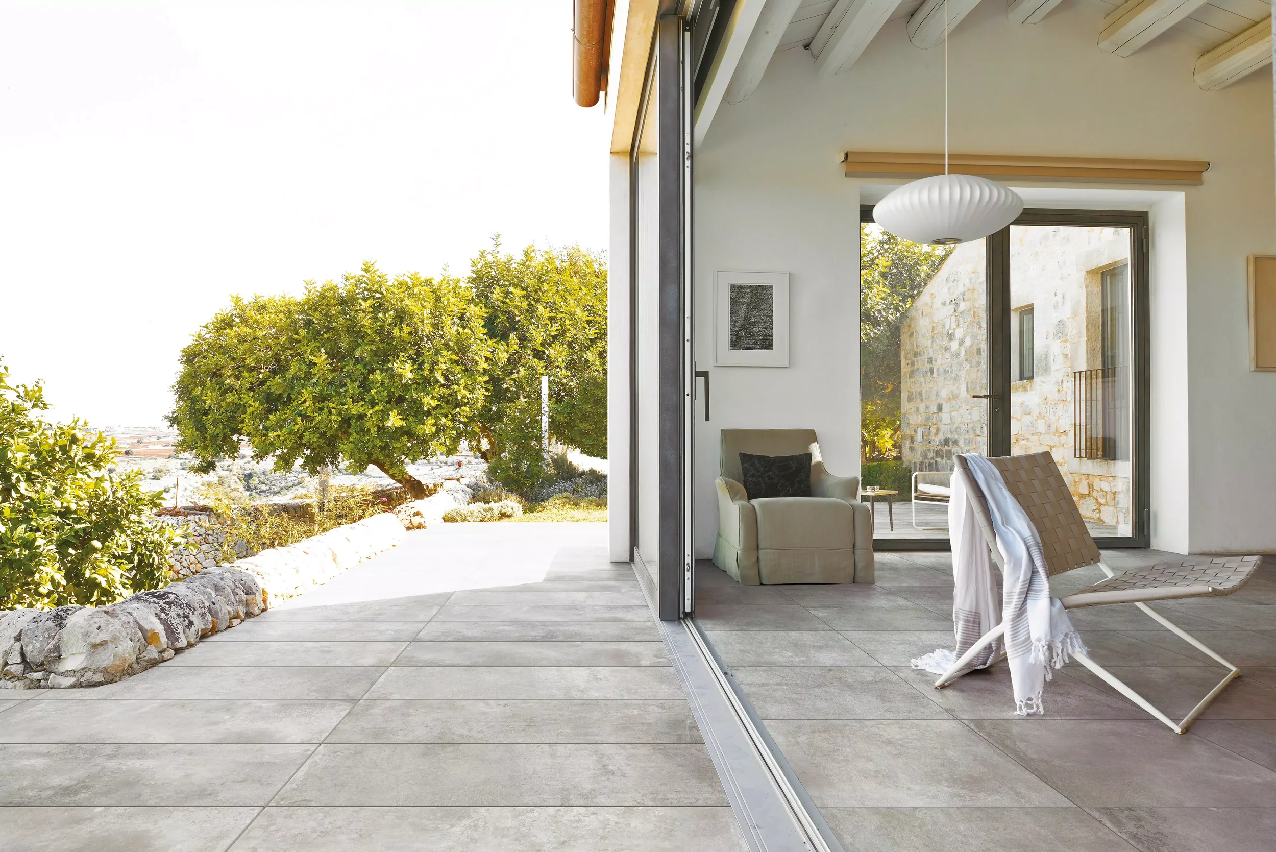 Seamless indoor-outdoor living space featuring La Roche Grey porcelain stoneware flooring by Florim, characterized by a matte finish and a neutral stone effect, expertly supplied and installed by PietraCasa.