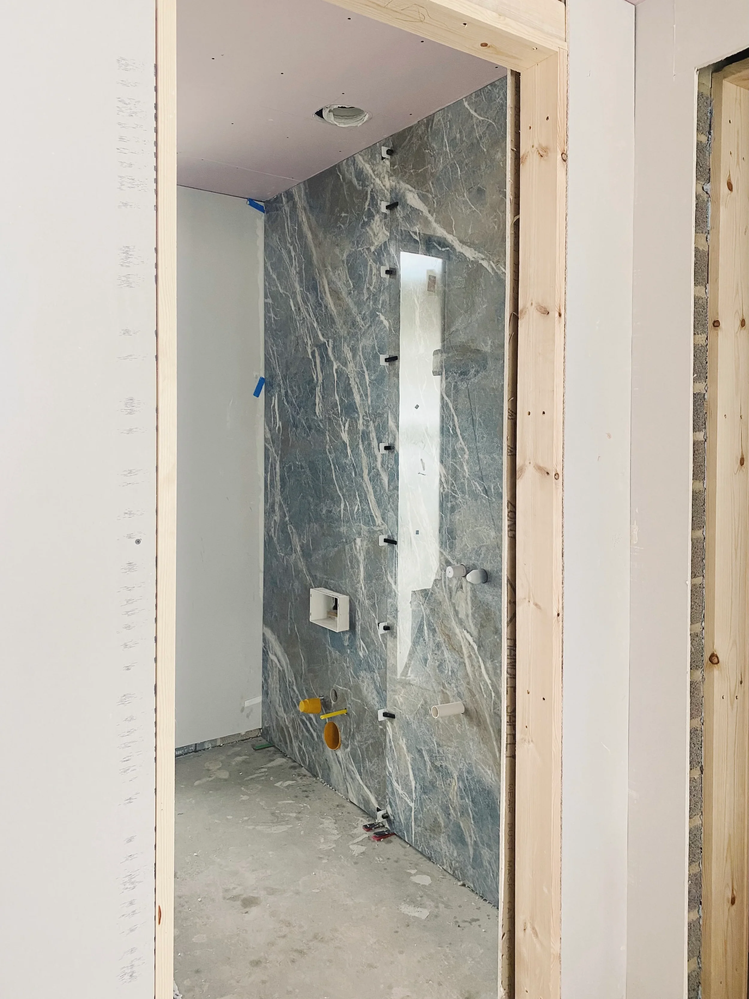 A high-end bathroom renovation under construction, featuring a striking, large-format porcelain feature wall with complex, dramatic veining that serves as a bold design statement