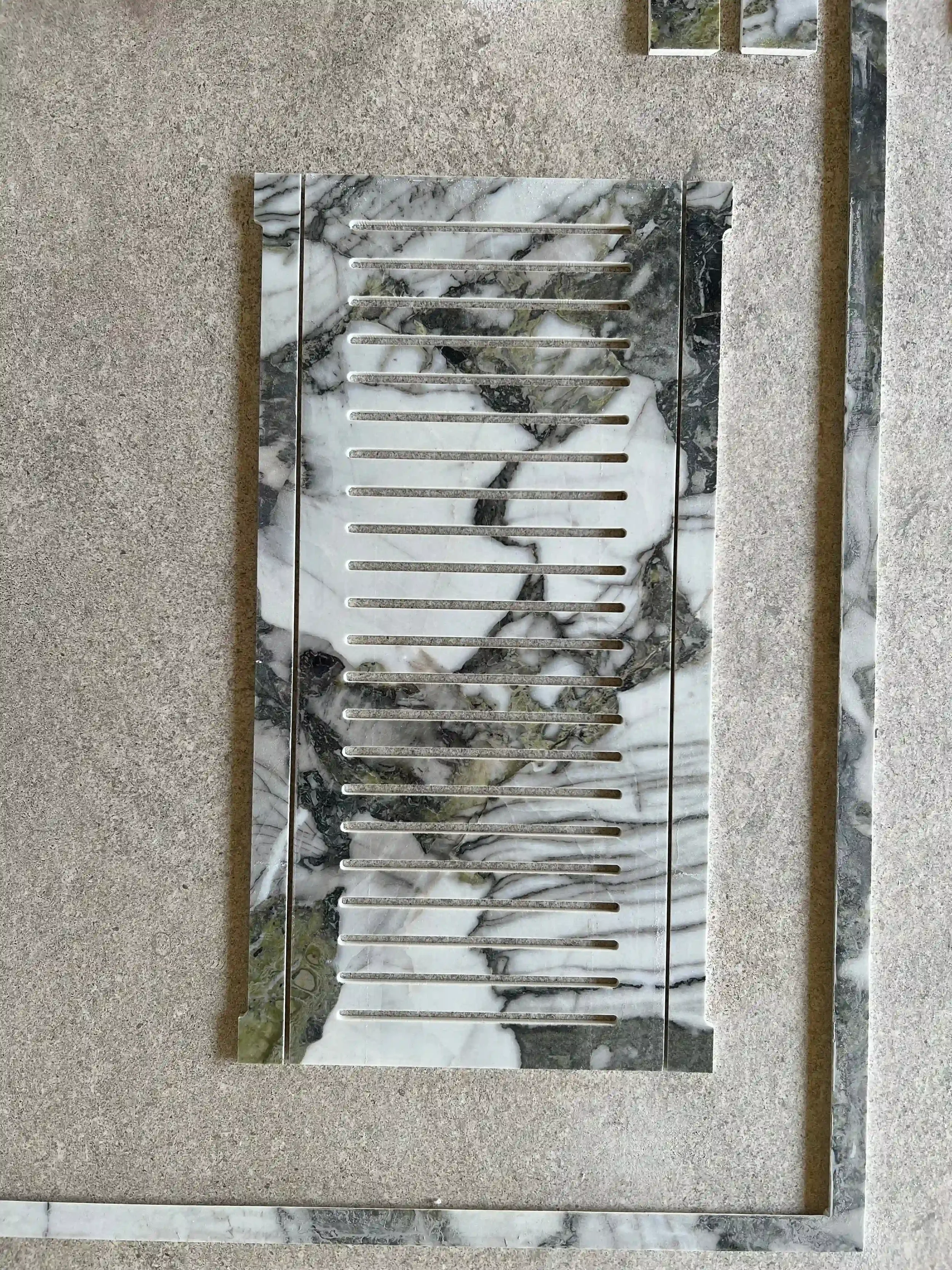 Custom waterjet cut linear shower grate featuring precision-cut horizontal slats fabricated from heavily veined luxury Calacatta Viola marble, integrated into a stone-effect porcelain tile floor by PietraCasa.