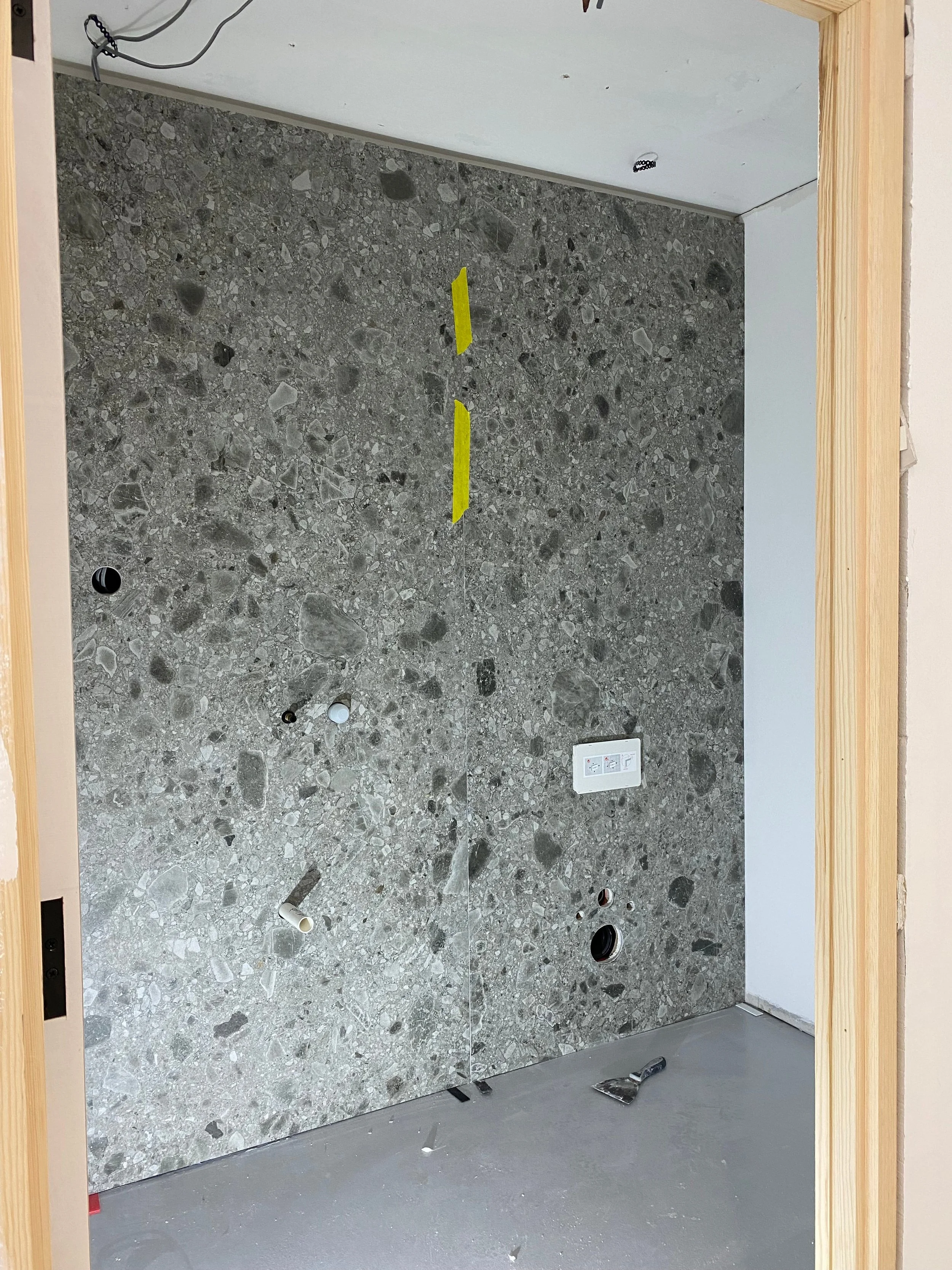 A high-end interior renovation showcasing a large-format, grey terrazzo-effect porcelain feature wall, currently under installation with seamless panel alignment.