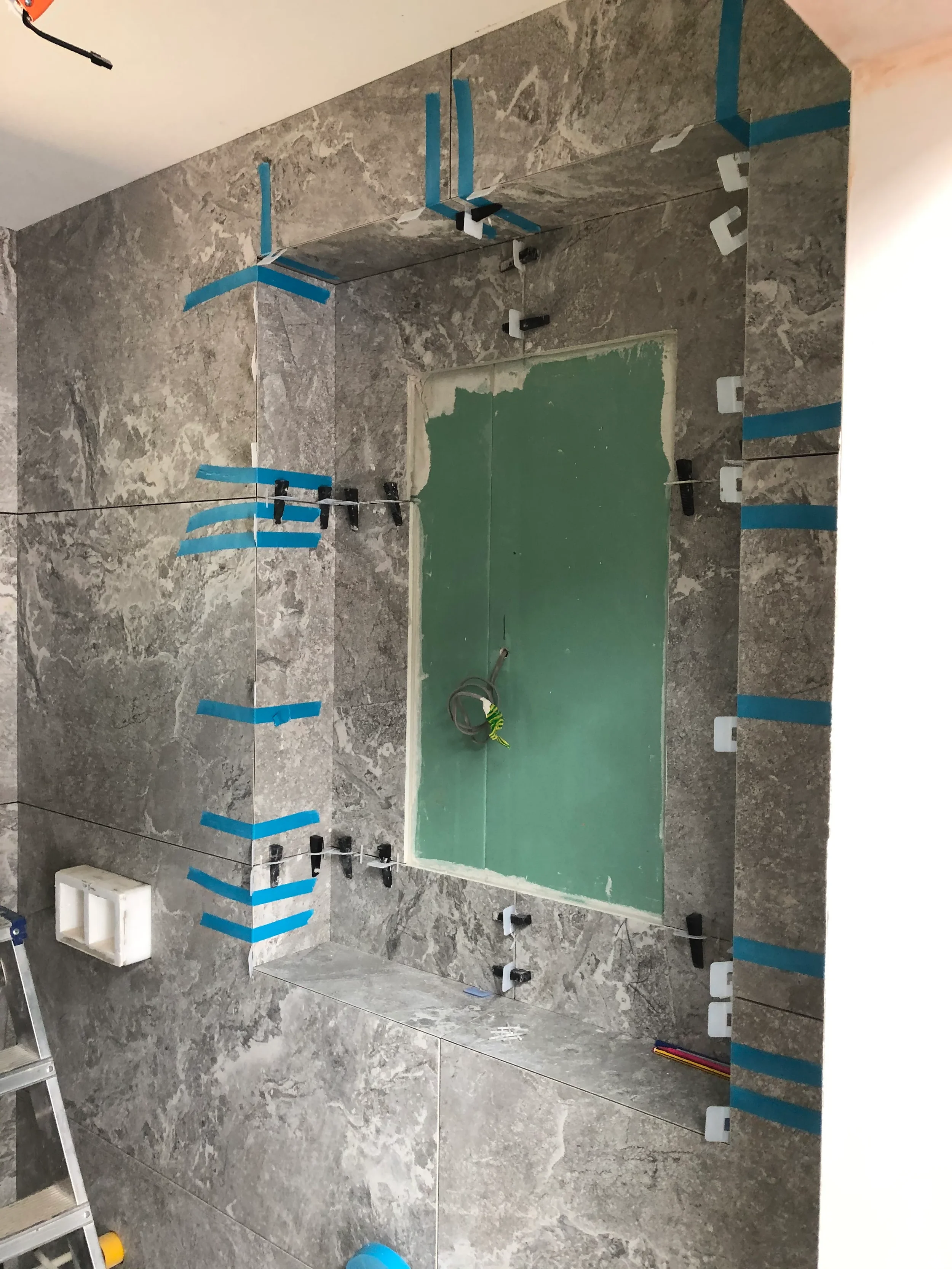 Installation of large-format grey marble-effect porcelain slabs around a recessed feature alcove.