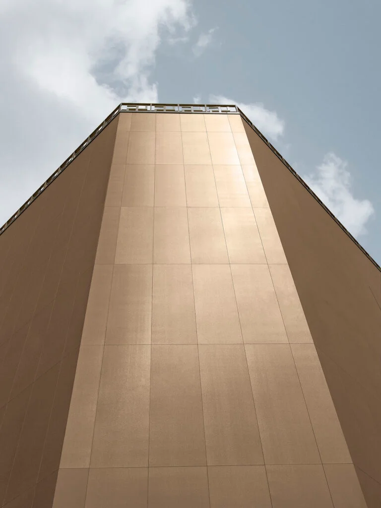 A building facade clad in Laminam Filo, a premium Italian architectural porcelain slab with a shimmering, bronze-gold metallic mesh texture, available through PietraCasa.