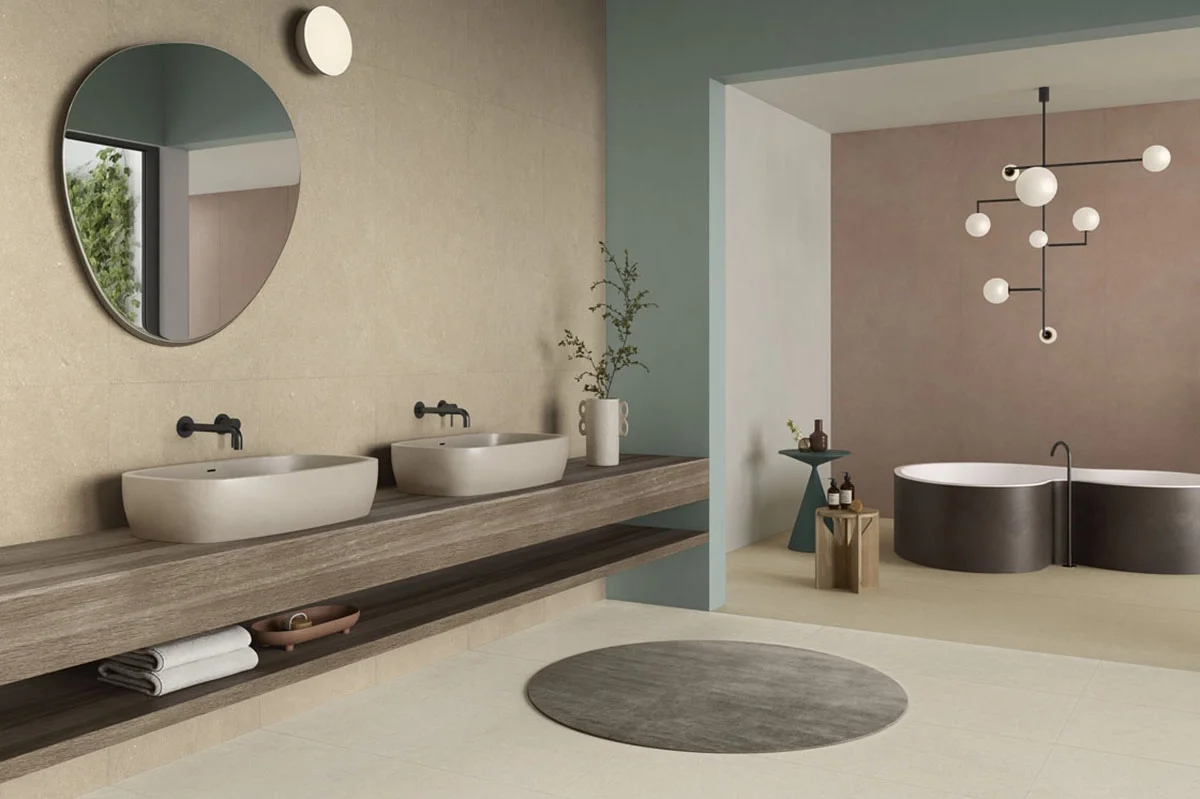 A tranquil, spa-like bathroom featuring Lea Ceramiche porcelain stoneware, showcasing limestone-inspired designs, a dark wood vanity, stone vessel sinks, and a deep soaking tub, available through PietraCasa.