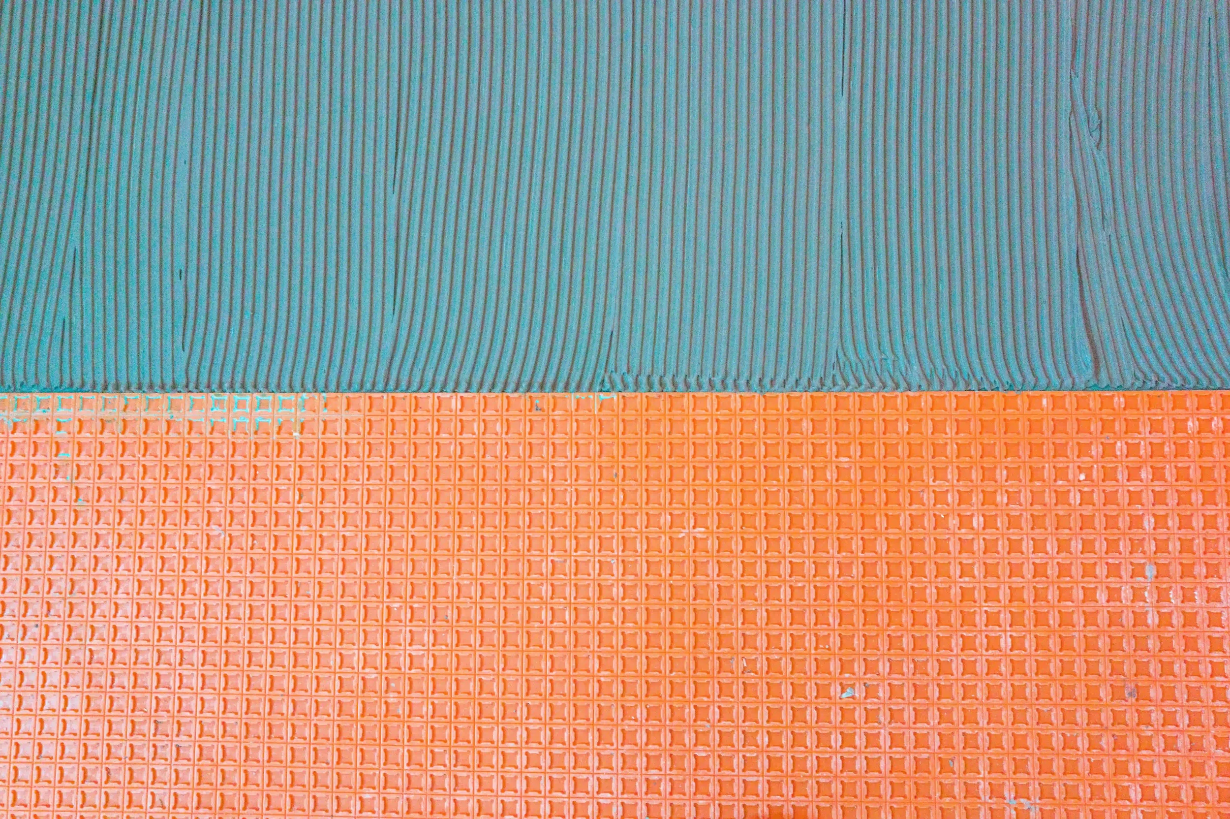 Combed tile adhesive being applied over an orange Schluter-DITRA flooring membrane.