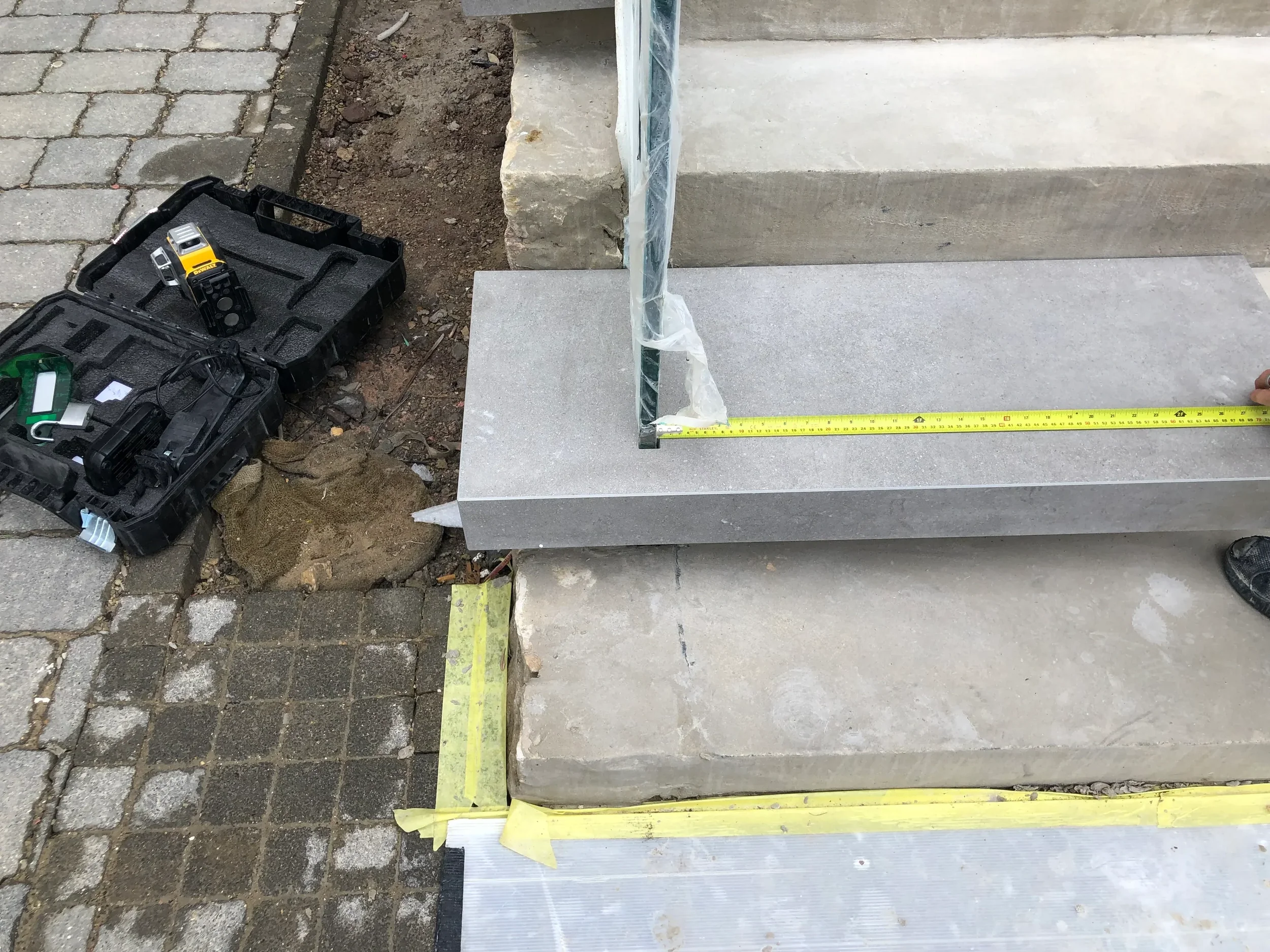 Exterior steps, showing a contractor measuring a precision-cut stone step with an integrated balustrade post during installation.