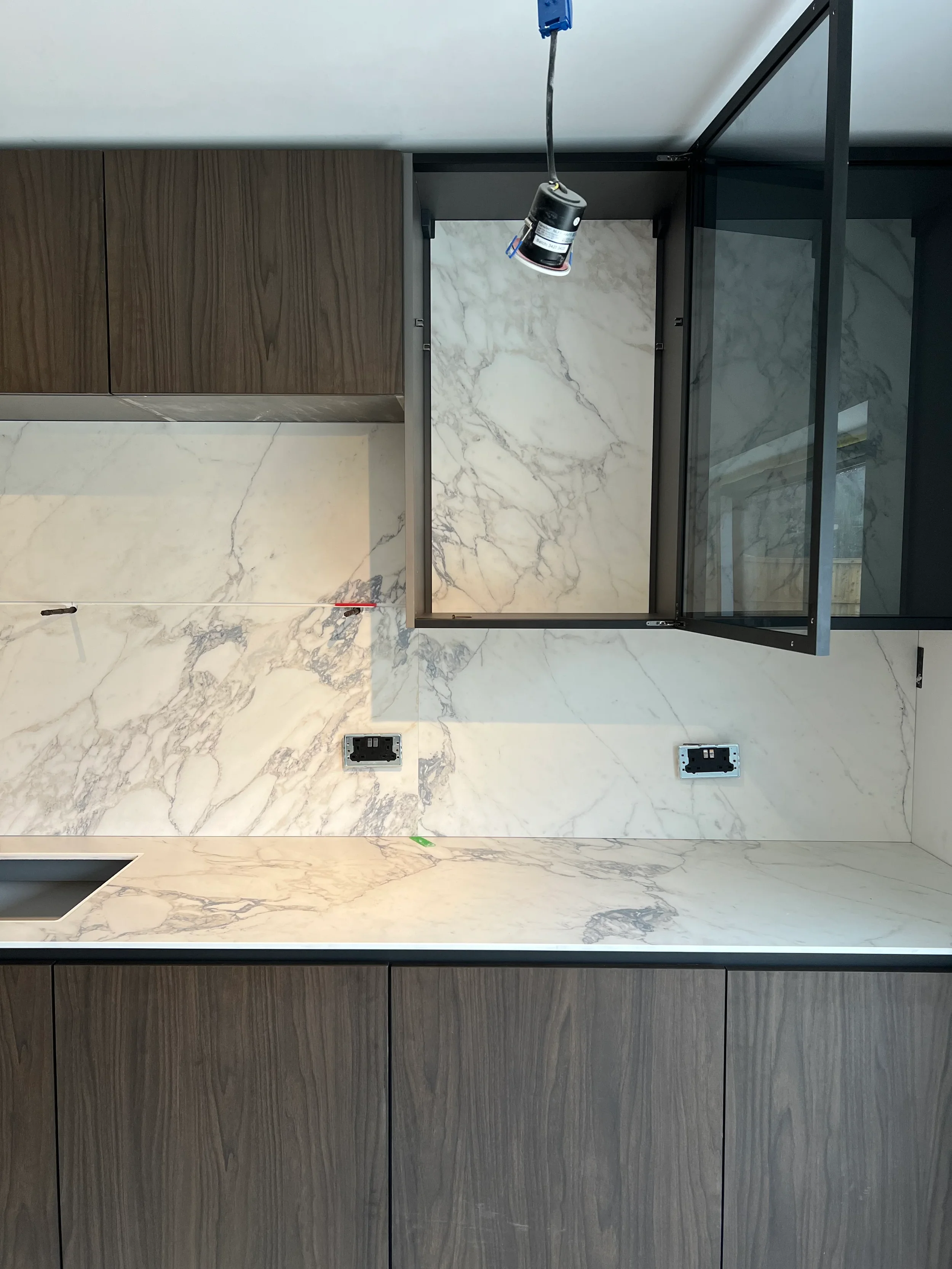 A high-end kitchen installation featuring seamless, large-format marble-effect porcelain worktops and full-height splashbacks, paired with dark wood cabinetry for a sophisticated, luxury aesthetic.