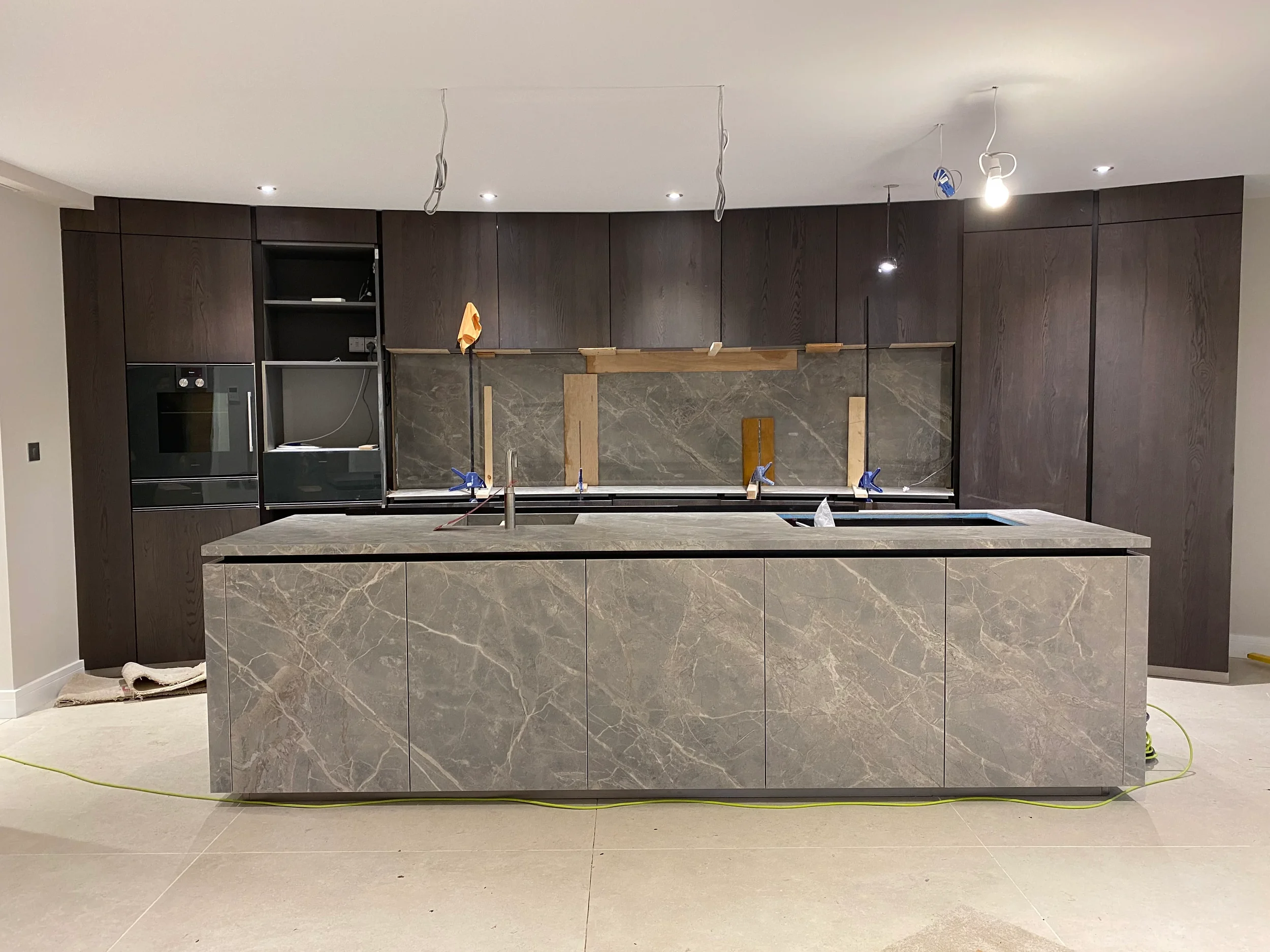 A luxury contemporary kitchen installation featuring a large central island entirely clad in bookmatched grey marble-effect porcelain panels by PietraCasa.