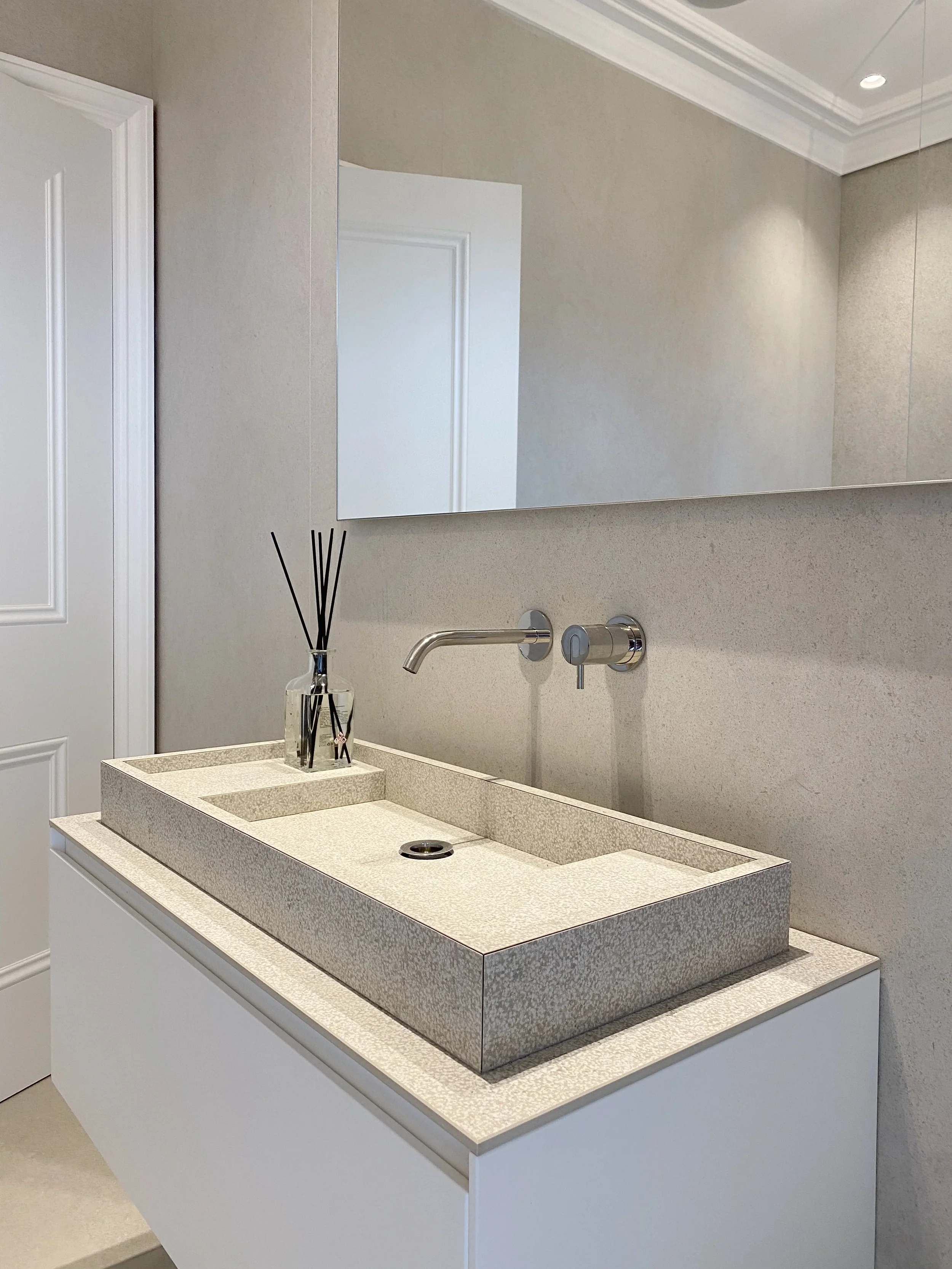 A sleek, modern vanity unit featuring a bespoke, integrated stone-effect porcelain sink, paired with a minimalist wall-mounted faucet for a clean, luxury aesthetic.