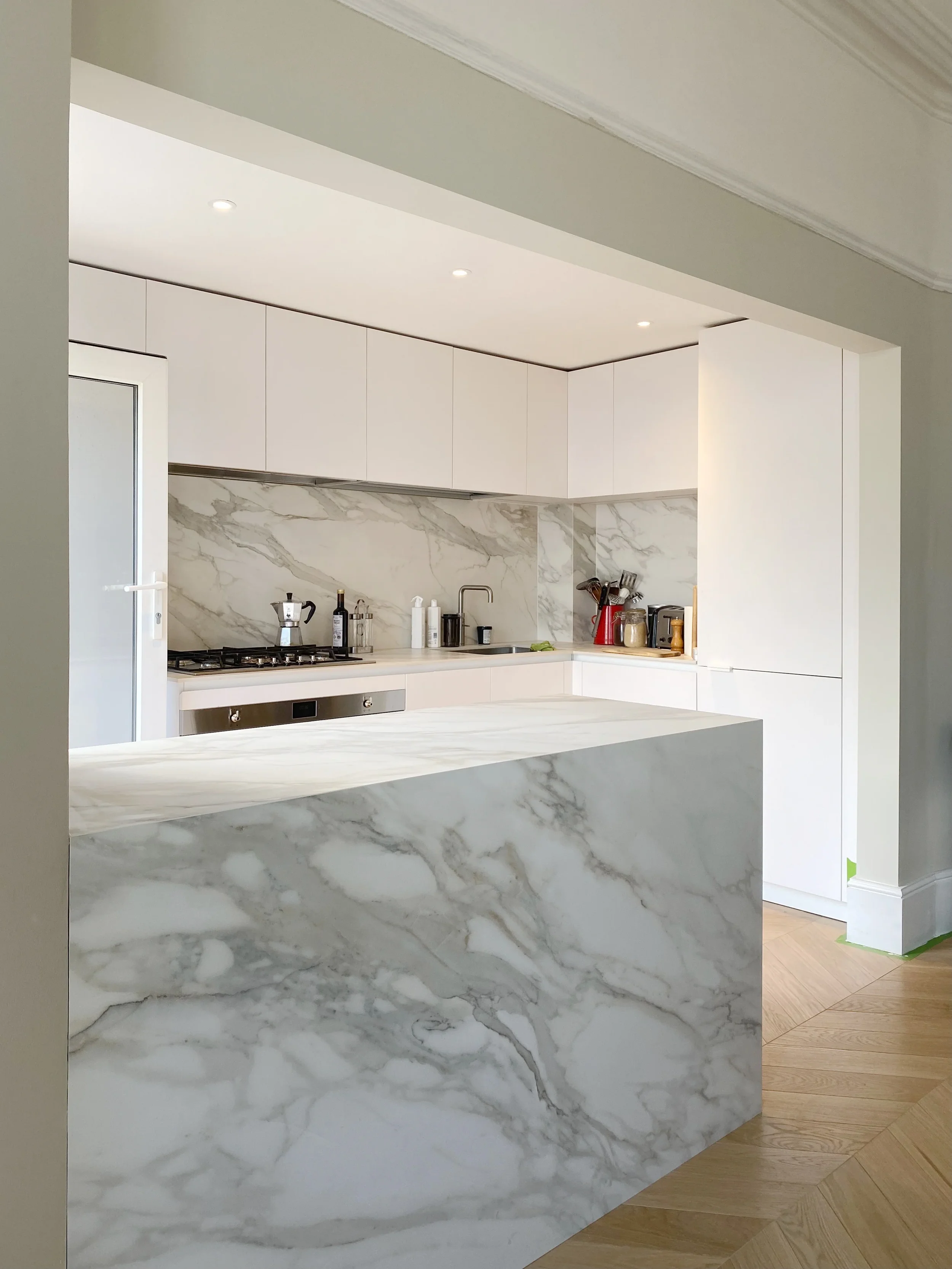 A high-end kitchen renovation featuring a bespoke-fabricated, marble-effect porcelain island and matching continuous splashback, showcasing precision mitred joinery and a luxurious, seamless aesthetic.