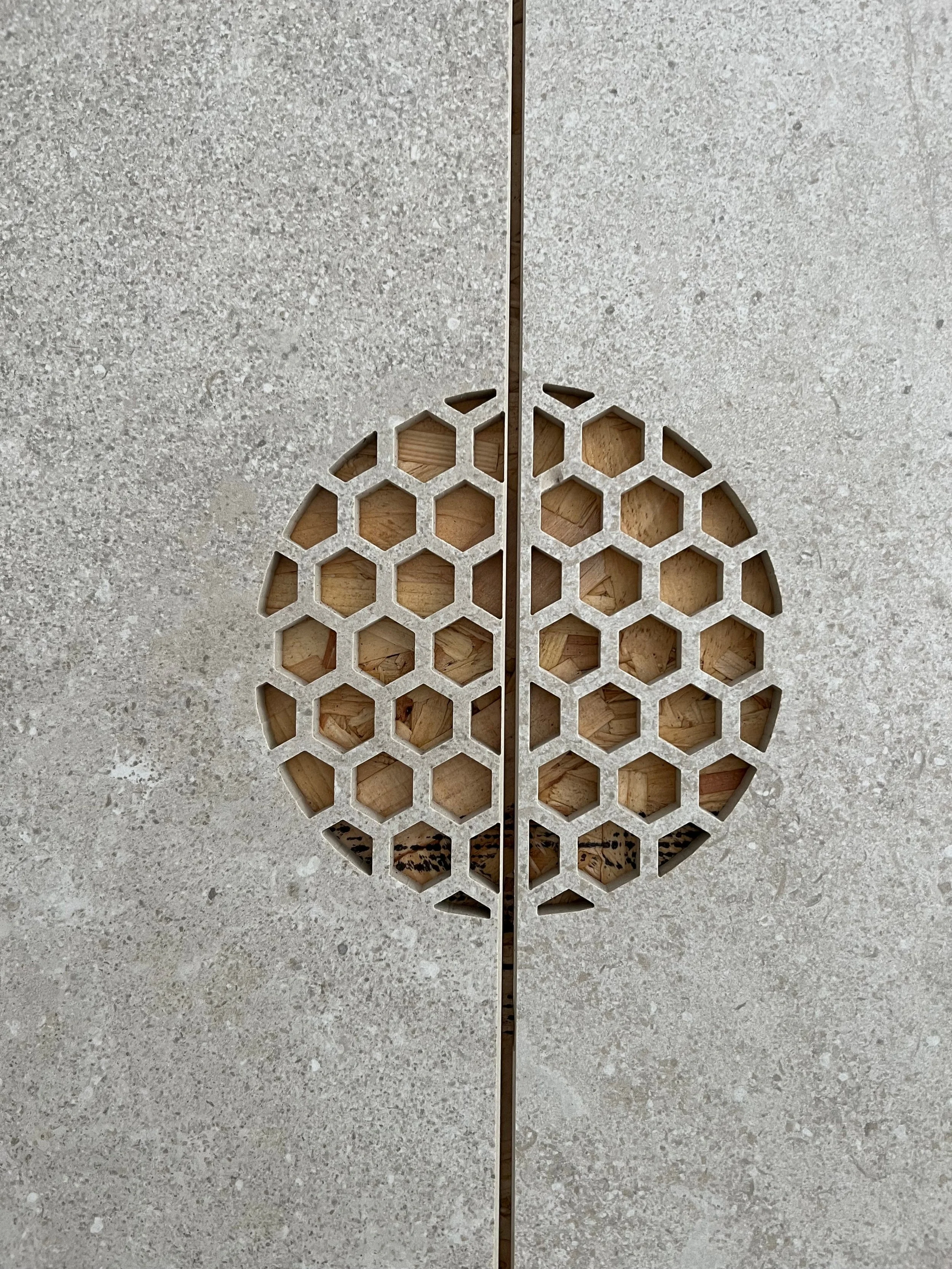 Two adjacent porcelain tiles featuring a precision waterjet cut circular drain split perfectly by a grout line, showcasing an intricate geometric hexagonal honeycomb pattern fabricated by PietraCasa.
