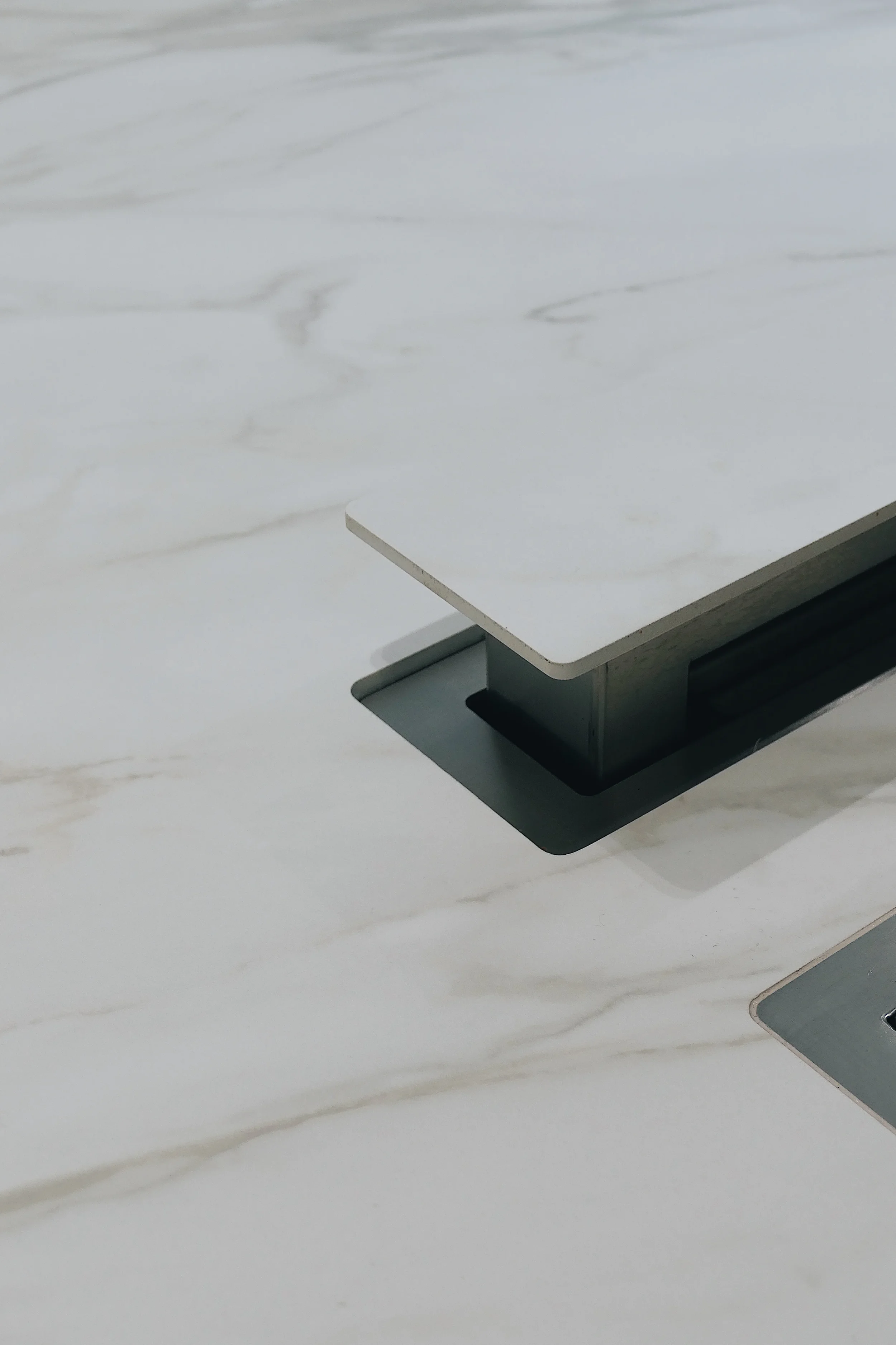 Close-up of a luxury kitchen island worktop custom fabricated from white marble-effect porcelain slabs, highlighting a seamlessly integrated downdraft extractor system clad with a matching porcelain top cap for a flawless, flush-fitting finish.